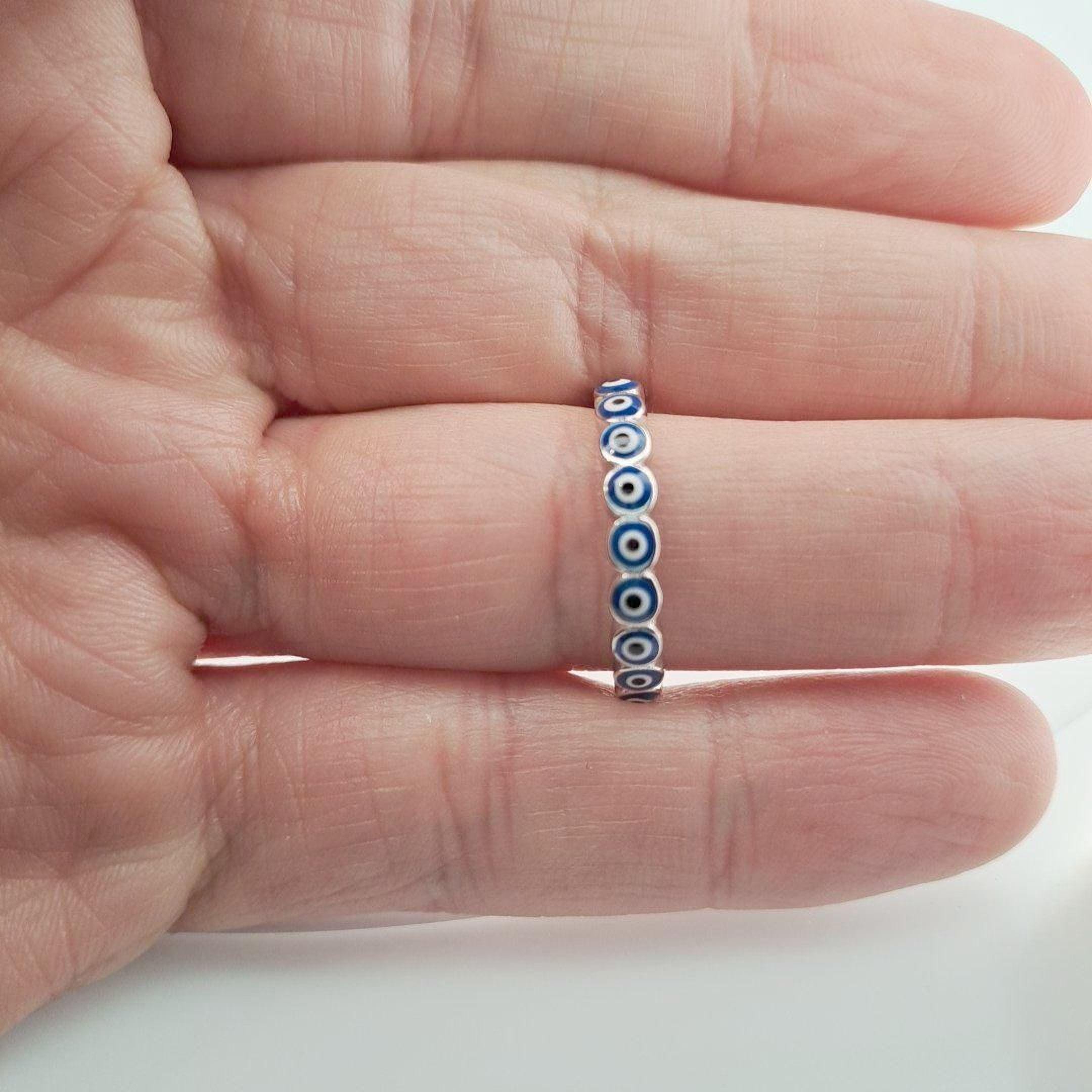 A hand is holding a silver ring with blue eye designs on it.