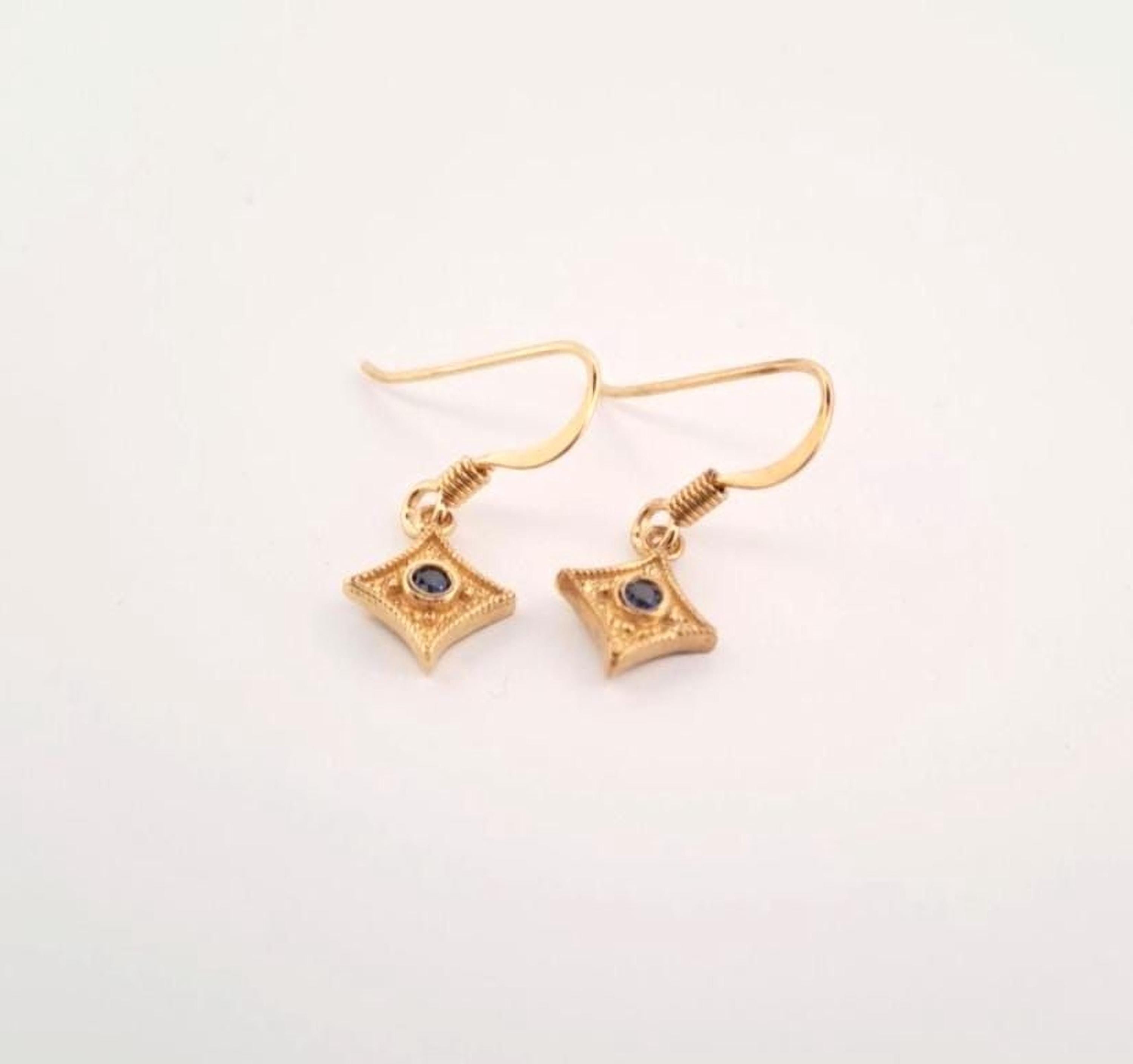 A pair of gold earrings with small blue gemstones on a white background.