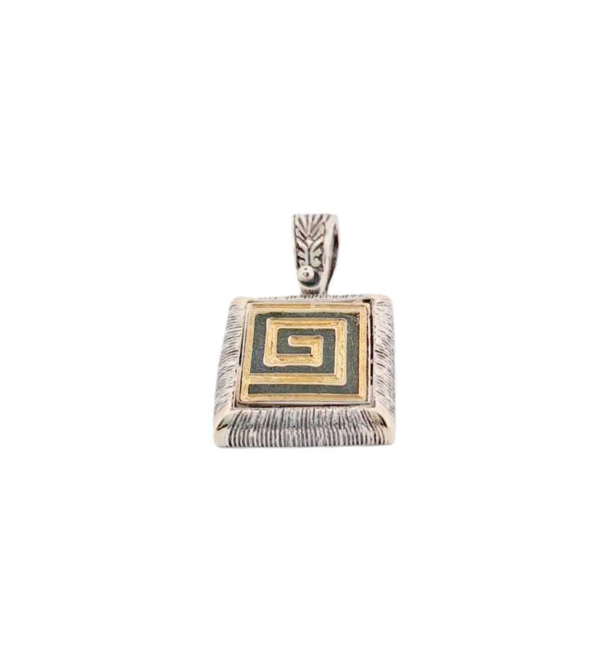 May include: Silver pendant with a square frame and a gold spiral design. The pendant has a textured edge and a decorative bail. The jewellery piece is likely a necklace pendant.