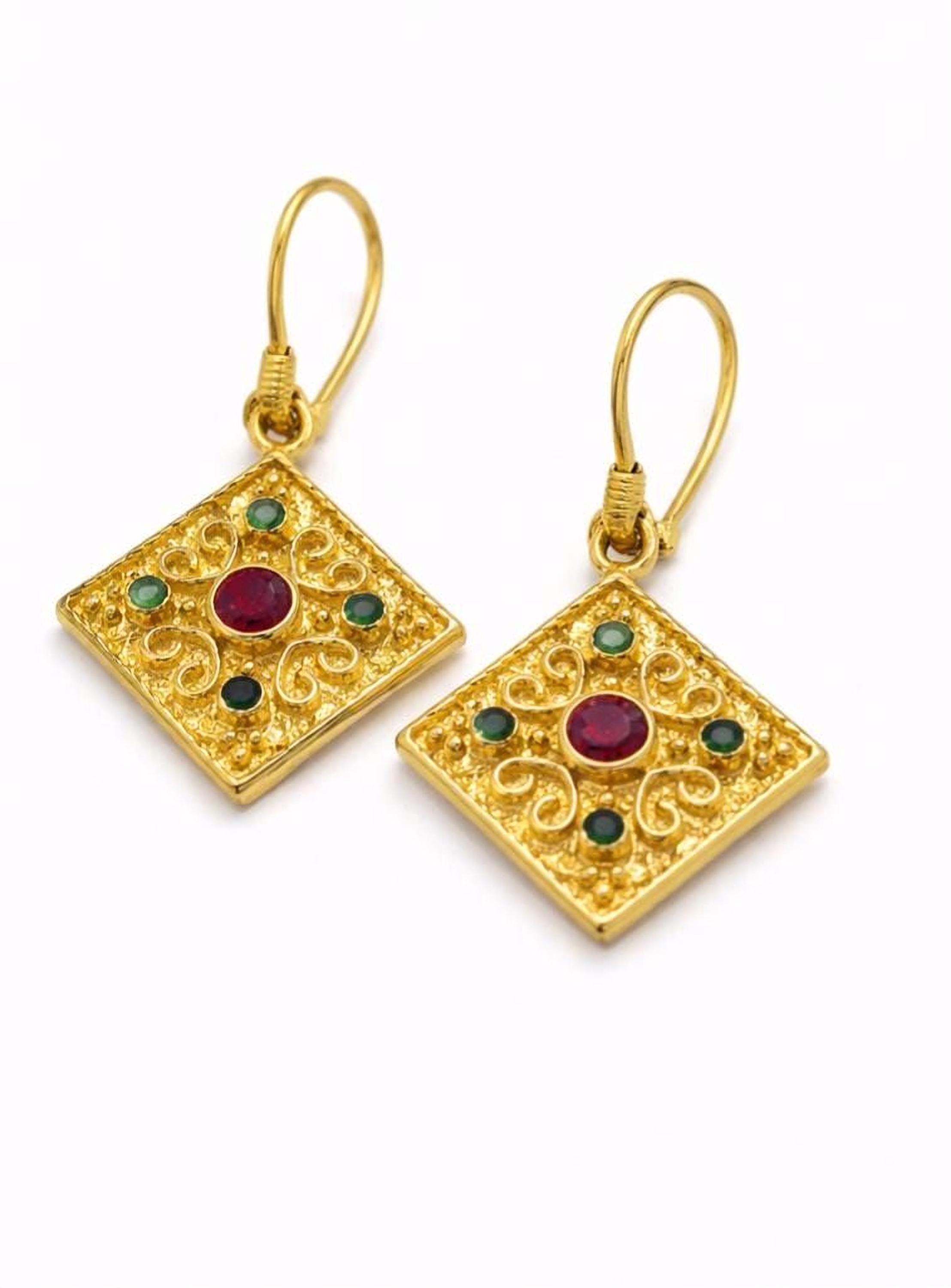a pair of gold earrings with a diamond-shaped design and a red gemstone in the center.