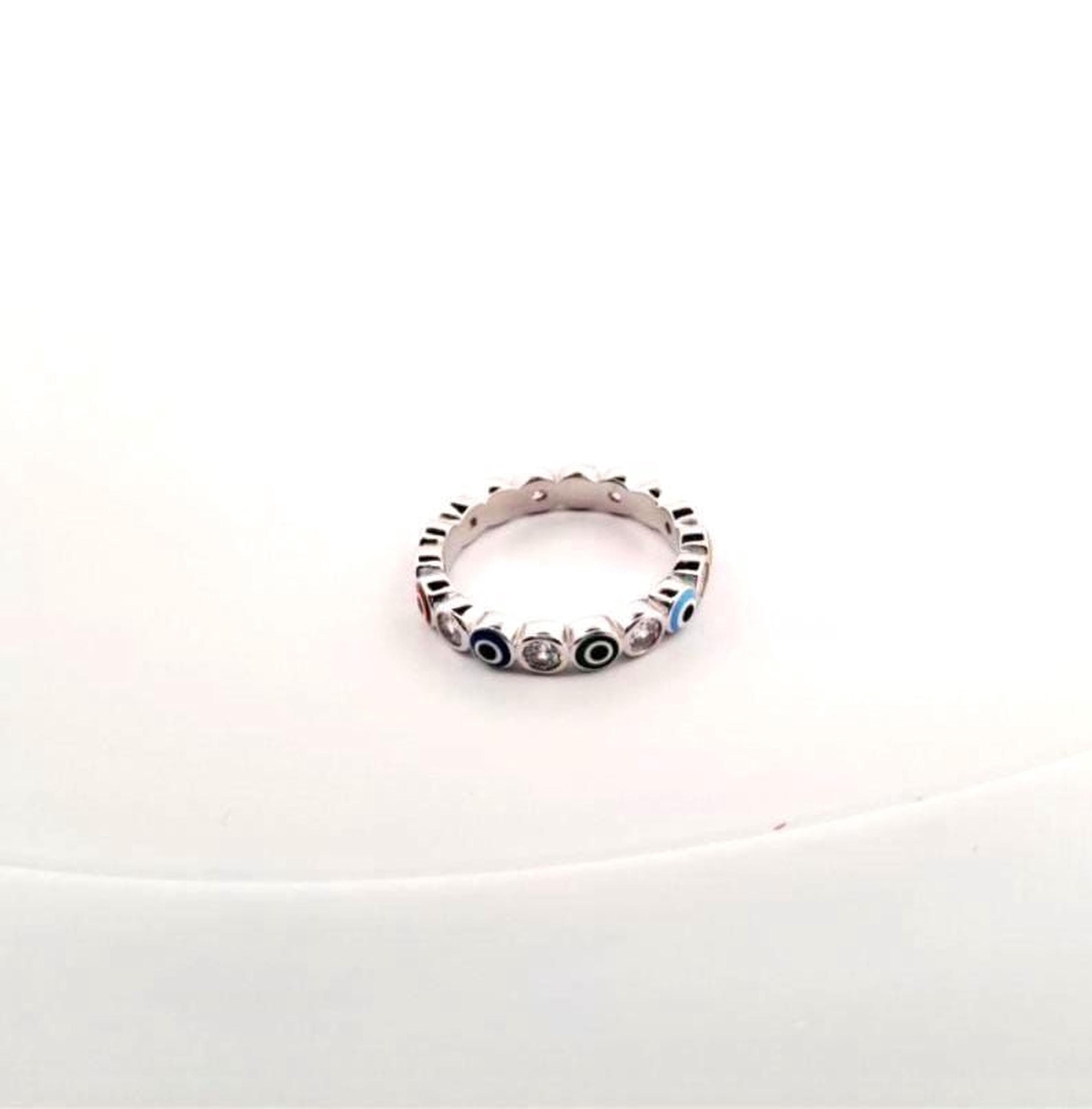 A silver ring with a row of colorful gemstones on it, placed on a white surface.