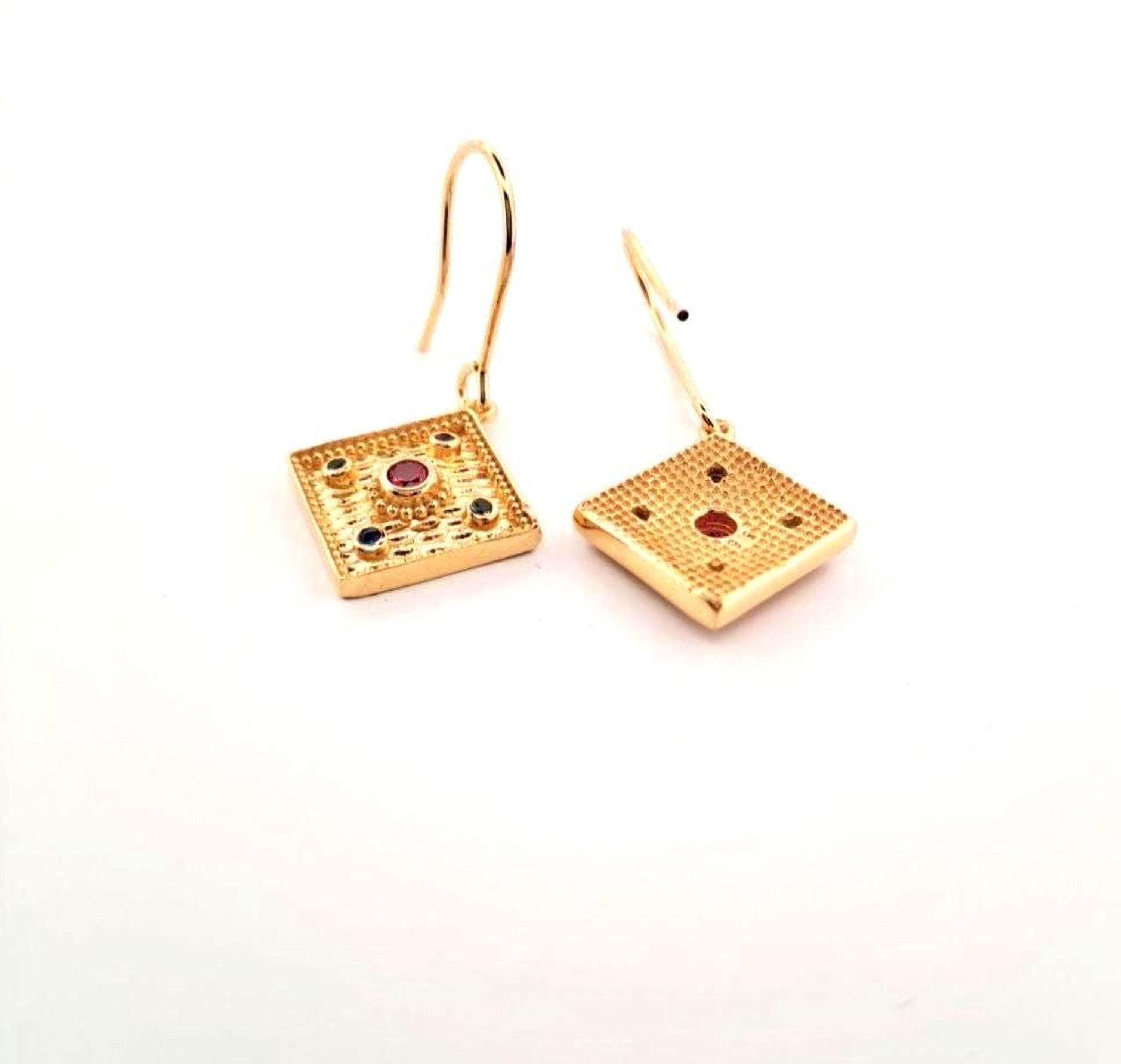 a pair of gold earrings with square designs, each featuring a gemstone.