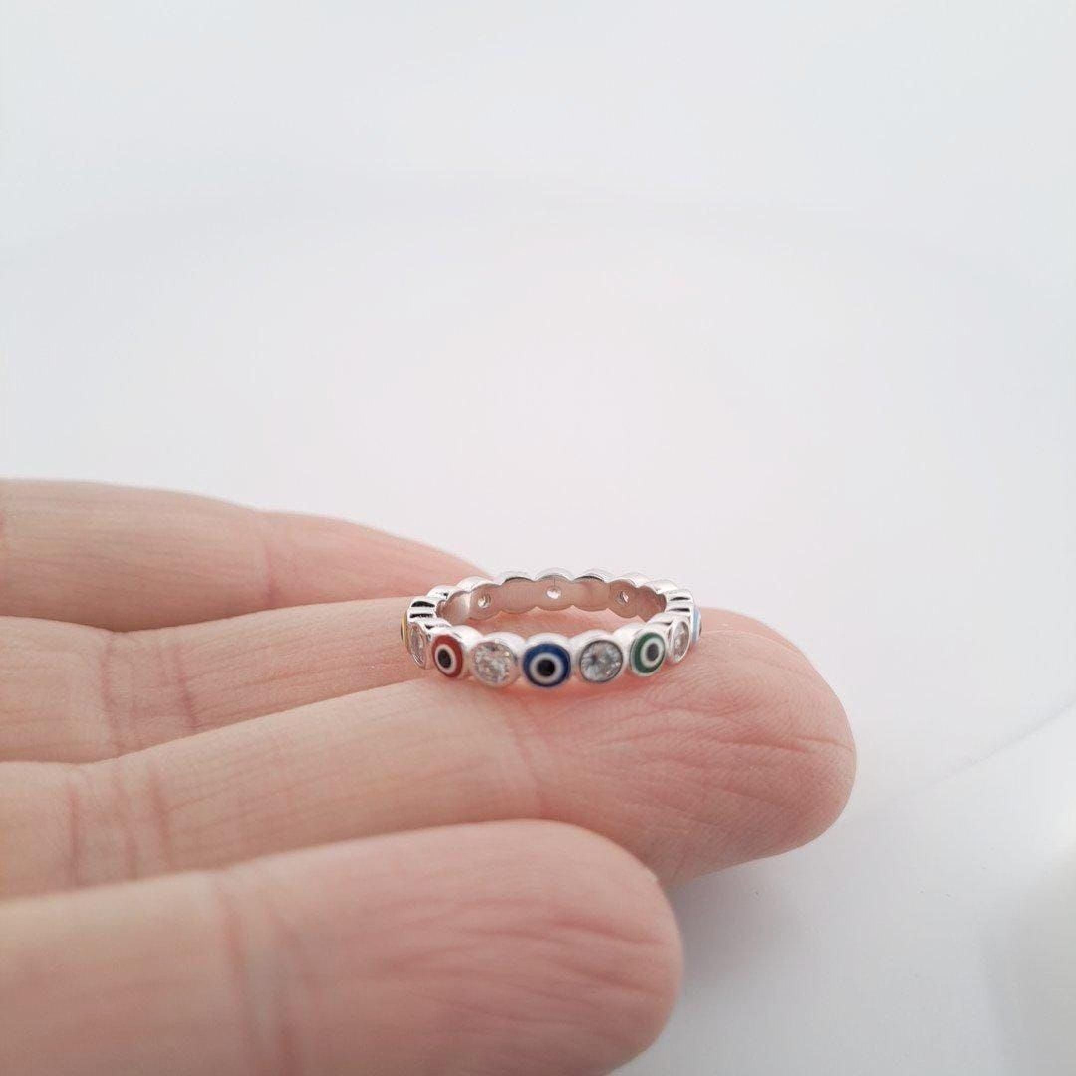 A hand is holding a silver ring with colorful gemstones on the fingers.