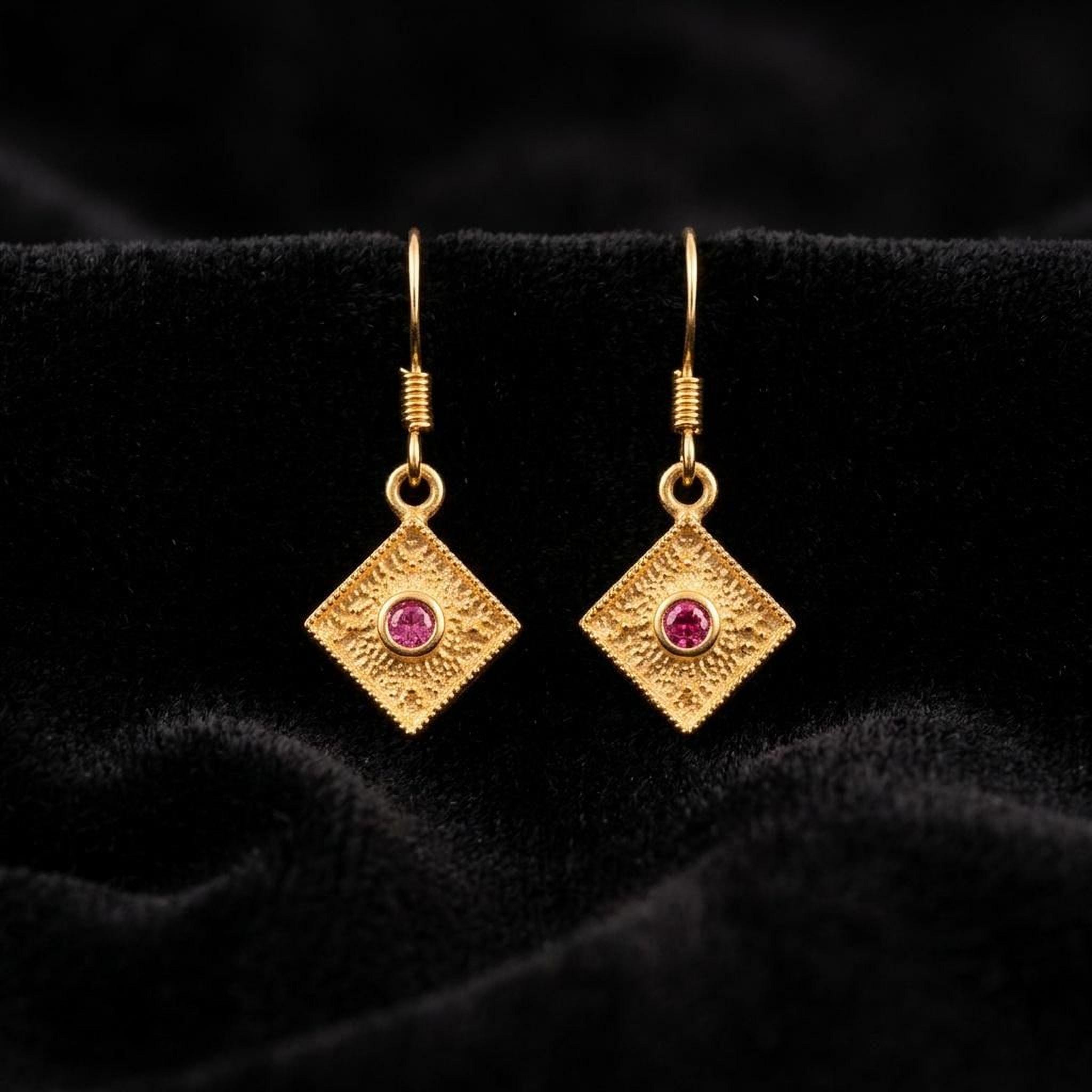 A pair of gold earrings with a pink gemstone, displayed on a black velvet background.