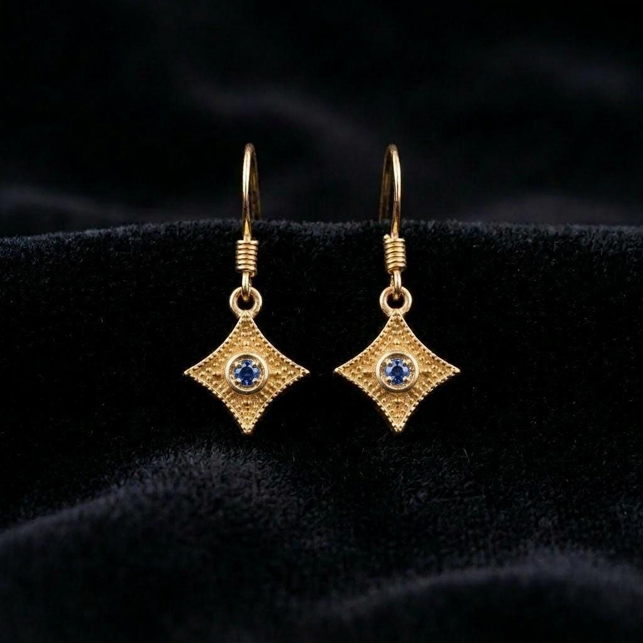 A pair of gold earrings with blue gemstones, displayed on a black velvet background.