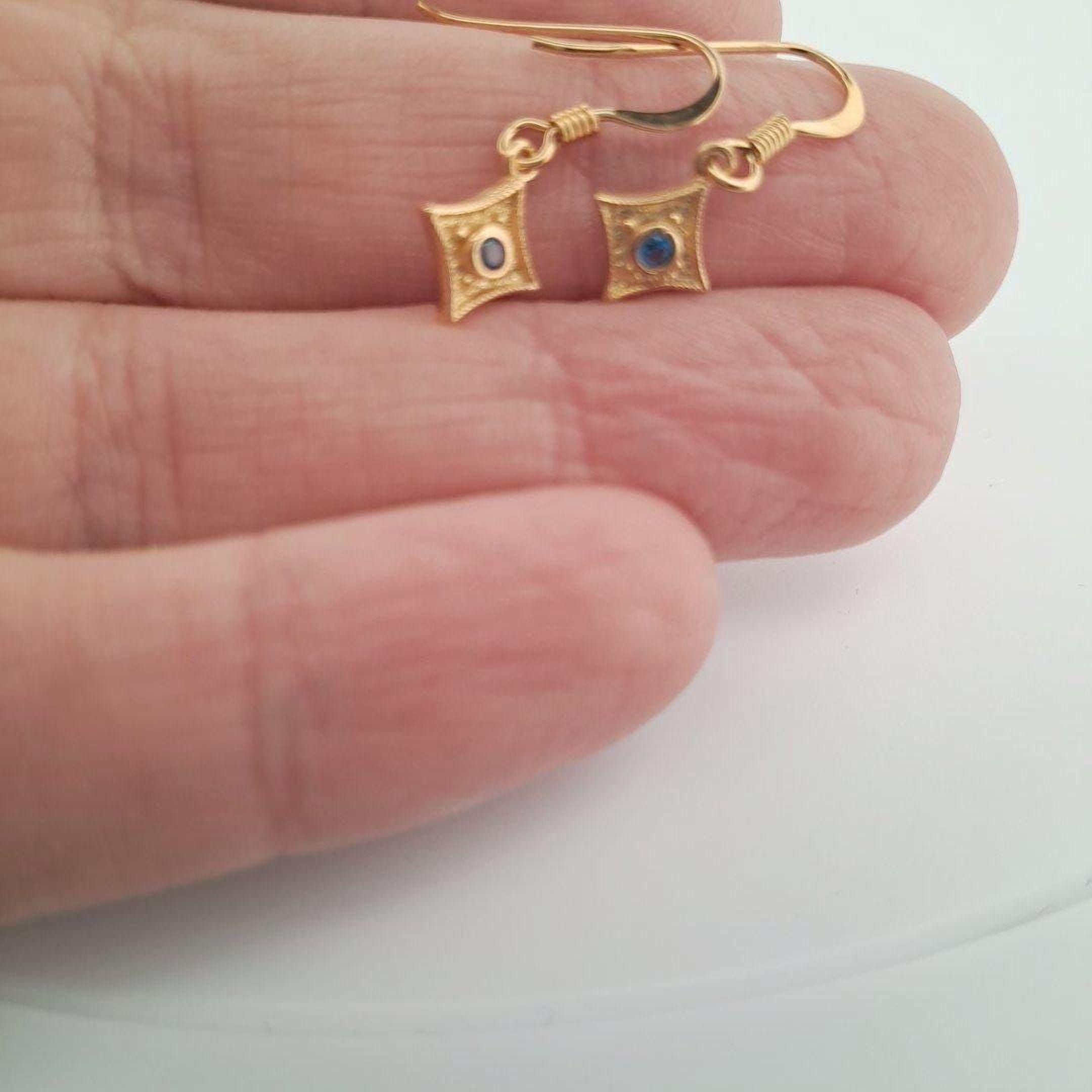 A pair of gold earrings with blue gemstones is being held in a person's hand.