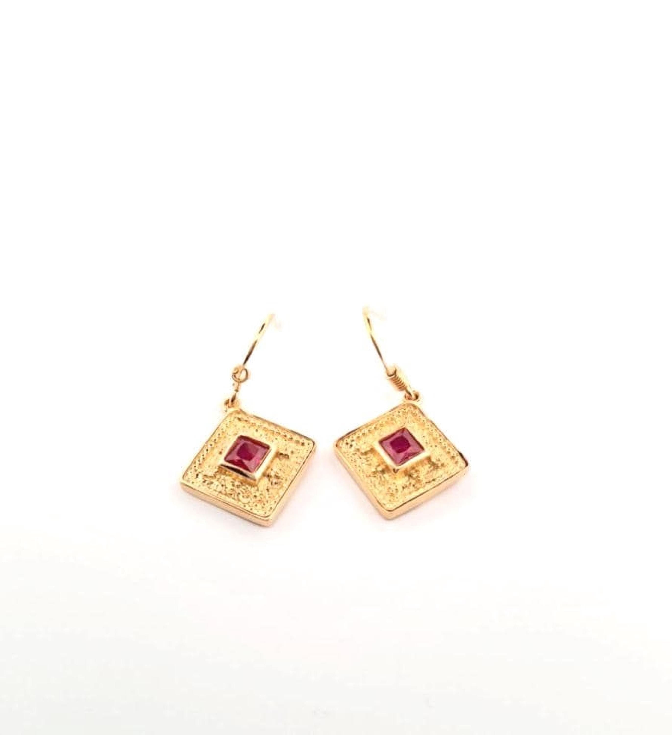 A pair of gold earrings with a red gemstone on a white background.