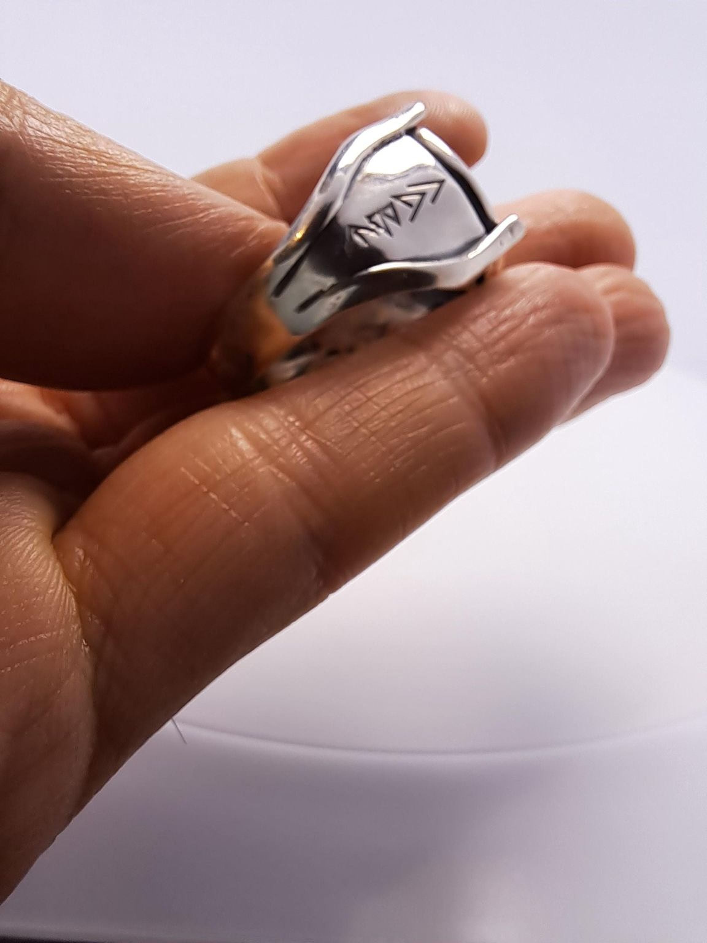 A person's hand holding a silver ring with an arrow design on it.