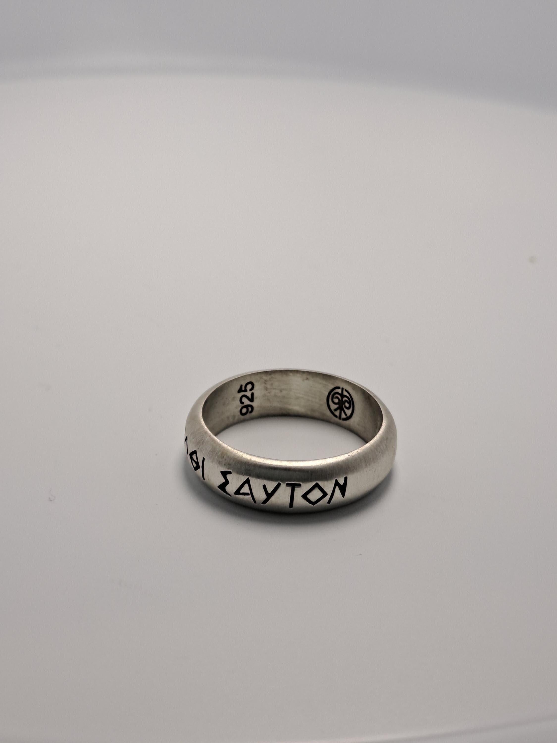 A silver ring with the name "AYTON" engraved on it, sitting on a plain white surface.