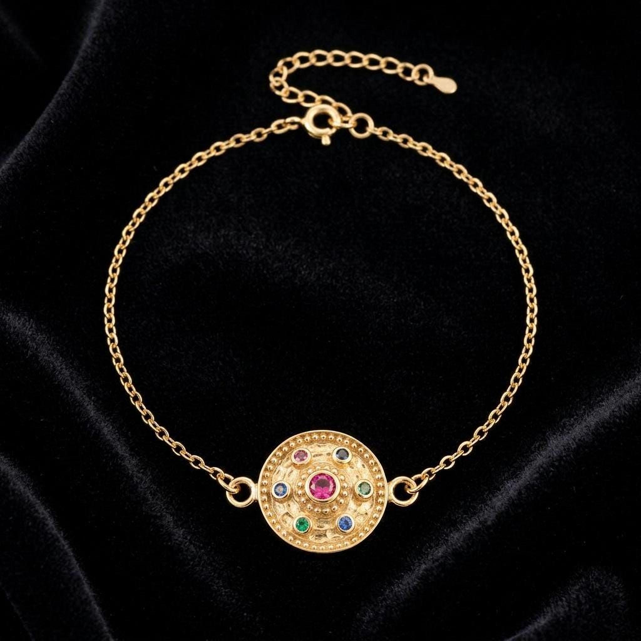A gold-colored bracelet with a circular medallion at the center, set against a black velvet background.