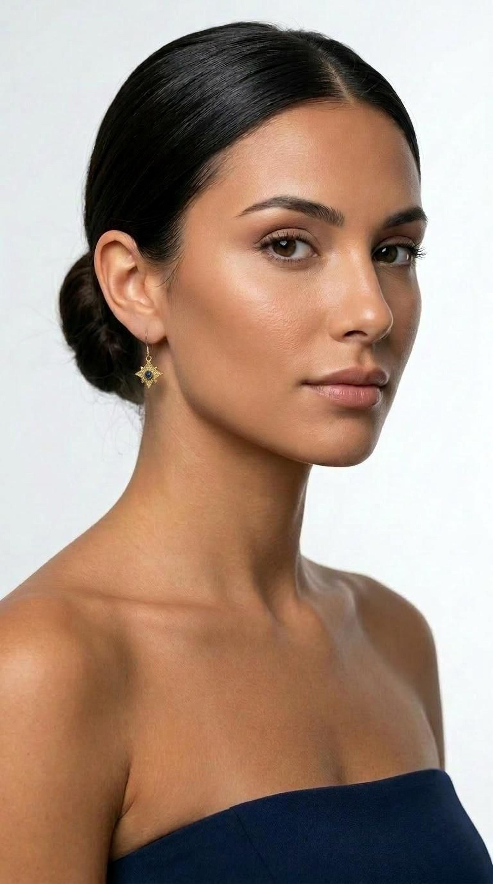 A woman with dark hair wearing a navy blue strapless top and a pair of gold star-shaped earrings.