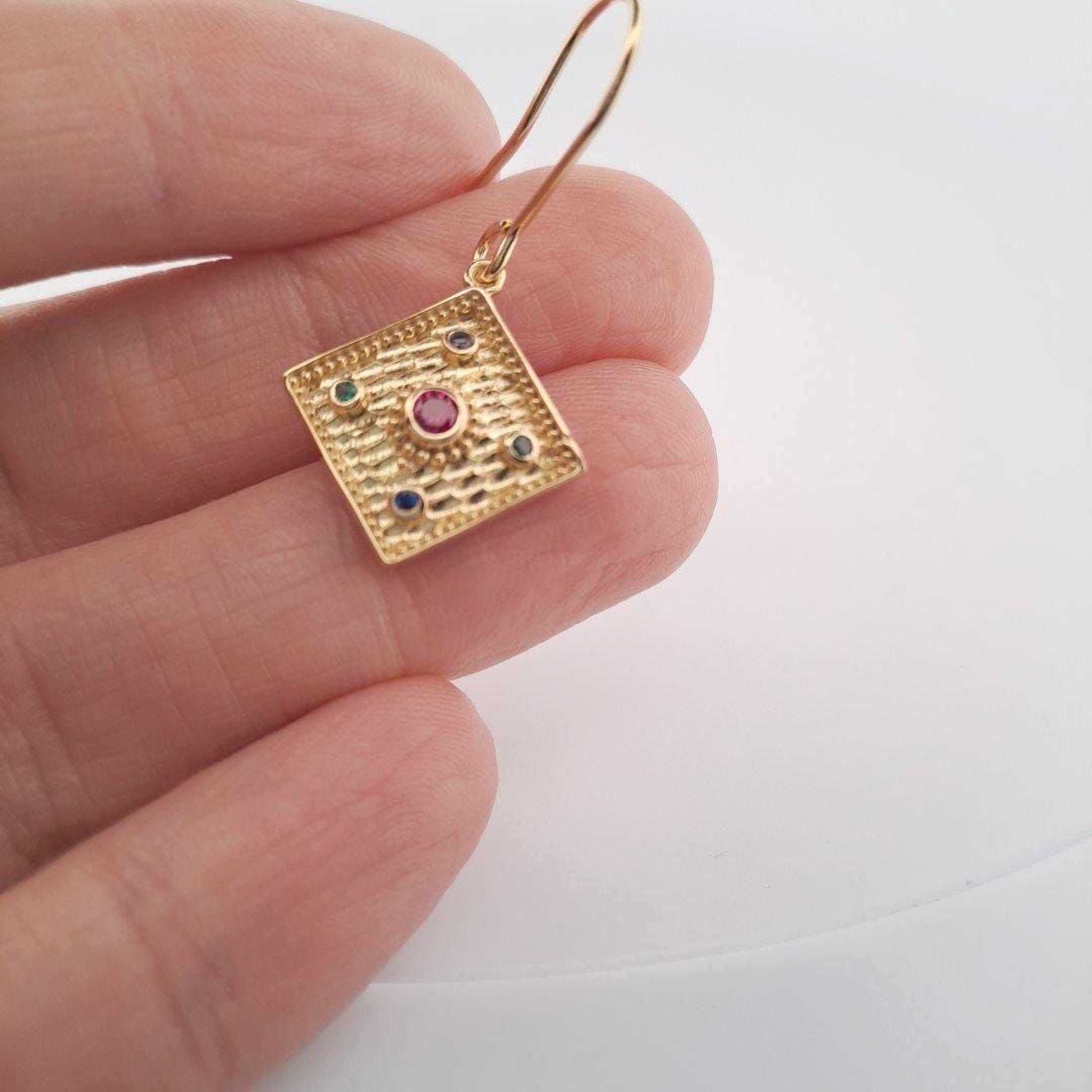 A hand holding a gold earring with a red gemstone in the center.
