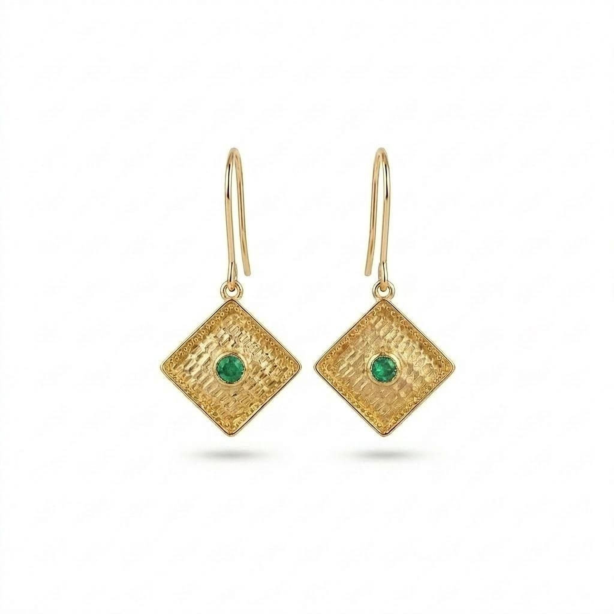 A pair of gold earrings with diamond-shaped designs and a green gemstone in the center.