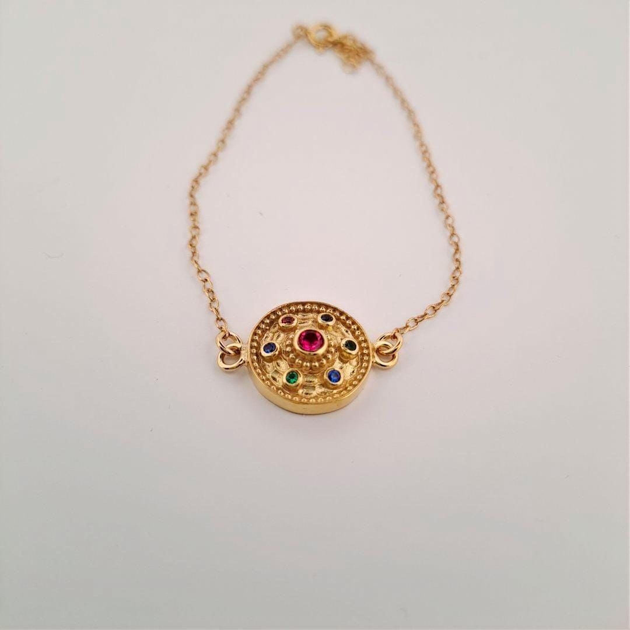 A gold-colored bracelet with a circular pendant featuring a variety of colorful gemstones.