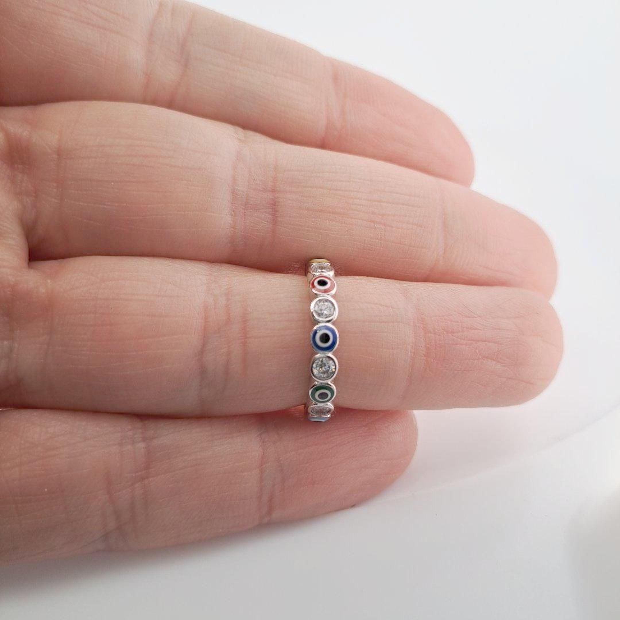 A hand is holding a ring with a row of colorful gemstones on the ring finger.