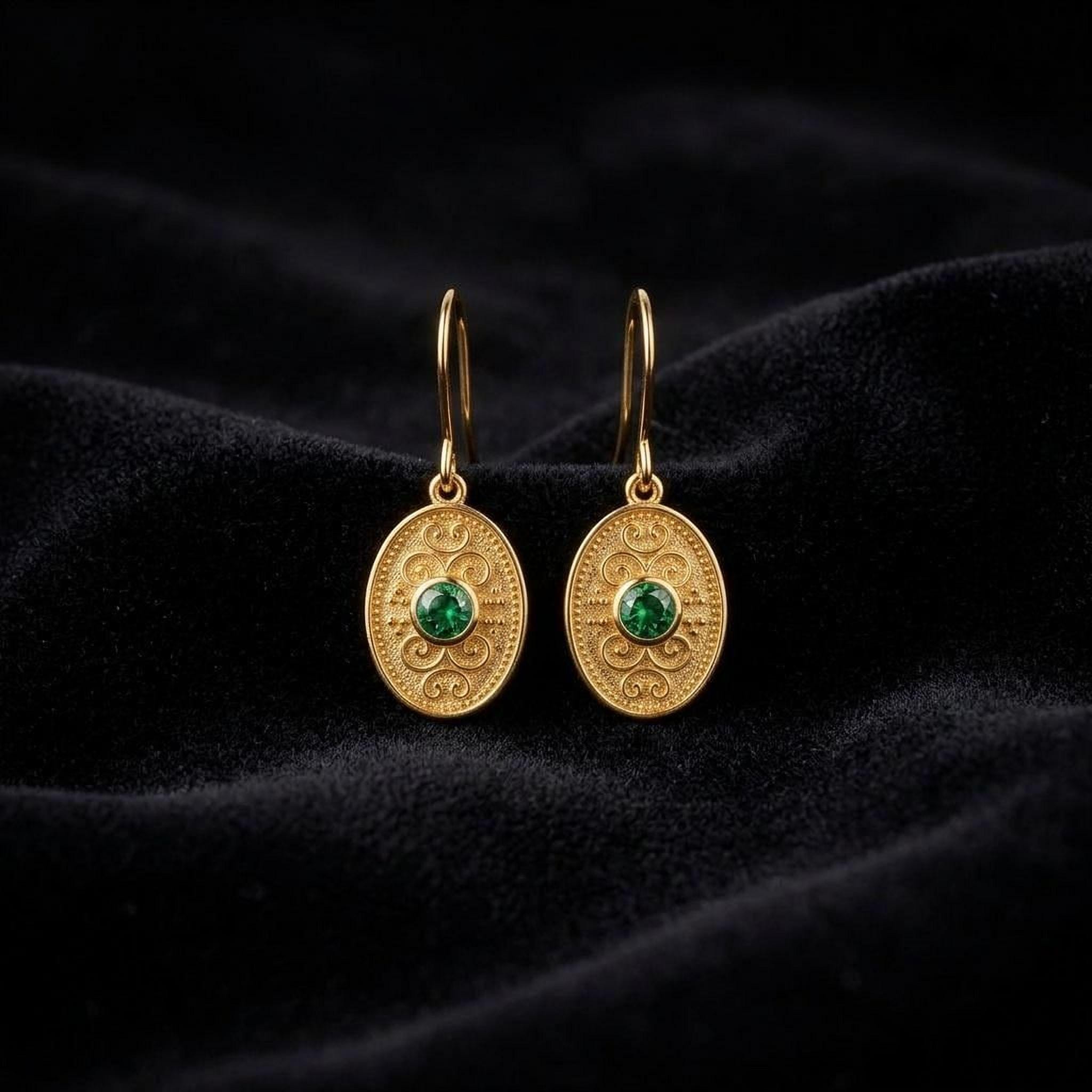 A pair of gold earrings with green gemstones, displayed on a black velvet background.
