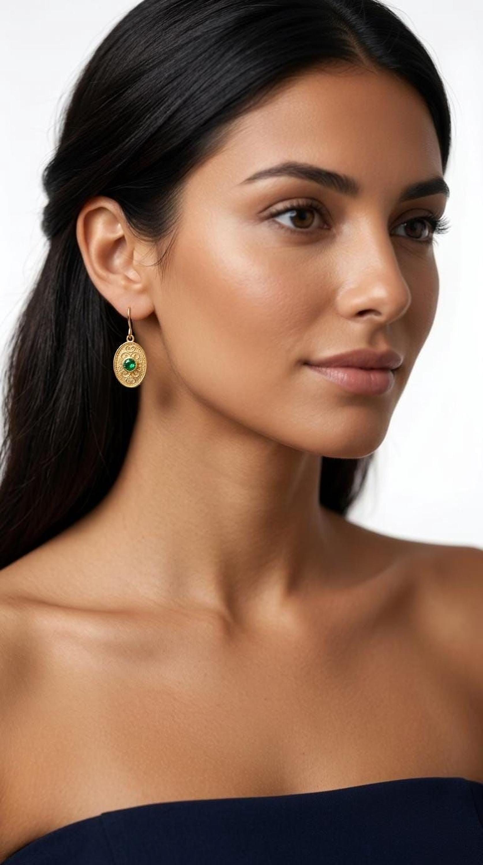 A woman with long dark hair wearing a gold earring with a green gemstone.
