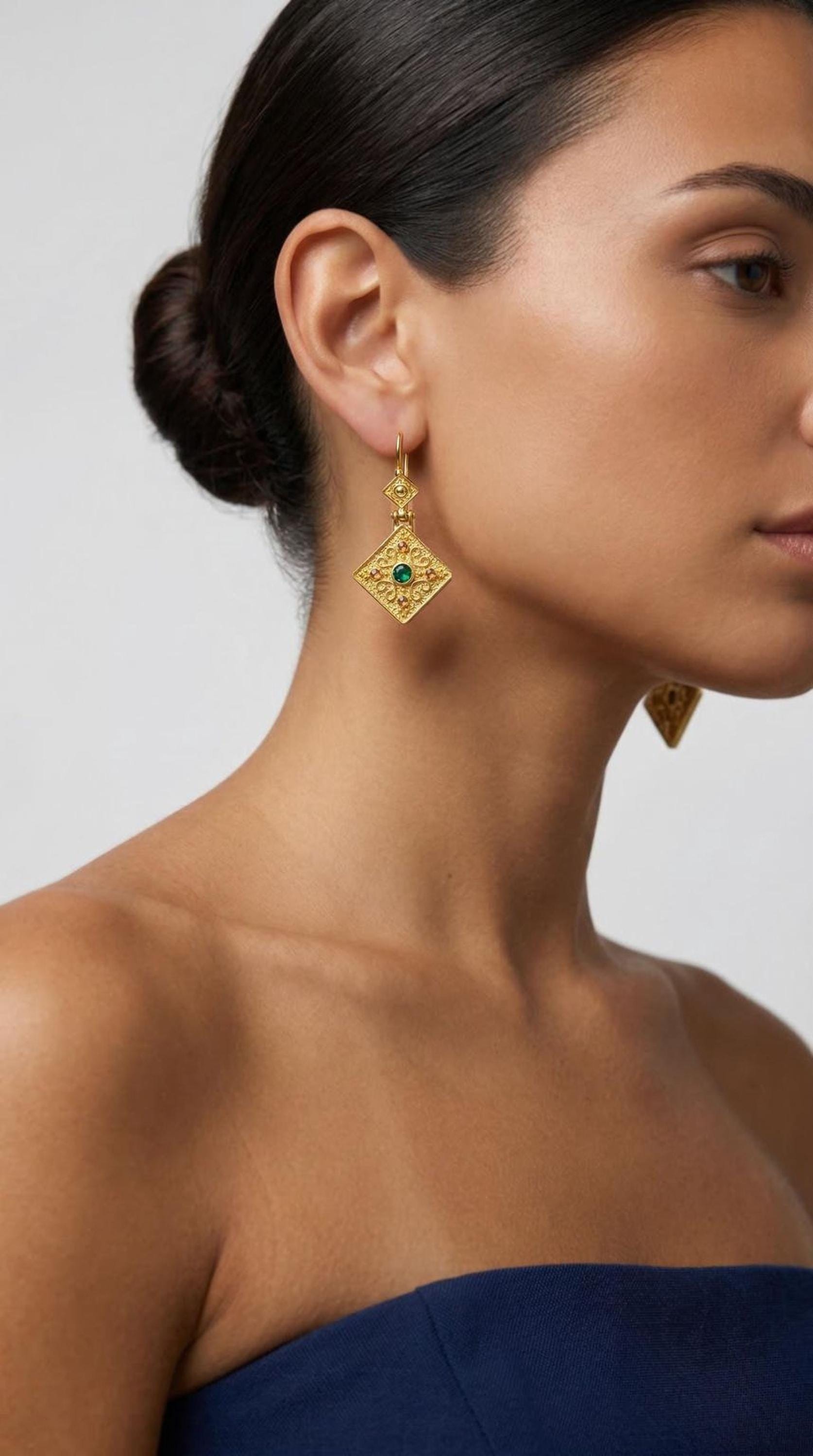 A woman wearing a pair of gold earrings with a green gemstone.
