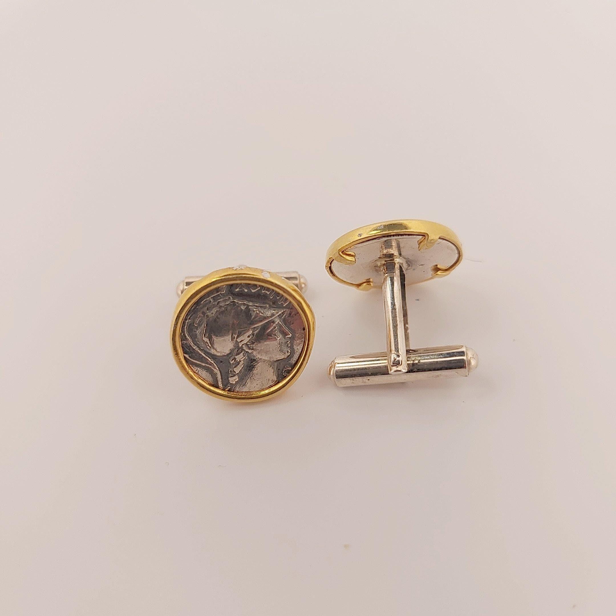 a pair of cufflinks with a coin-like design, placed on a white background.
