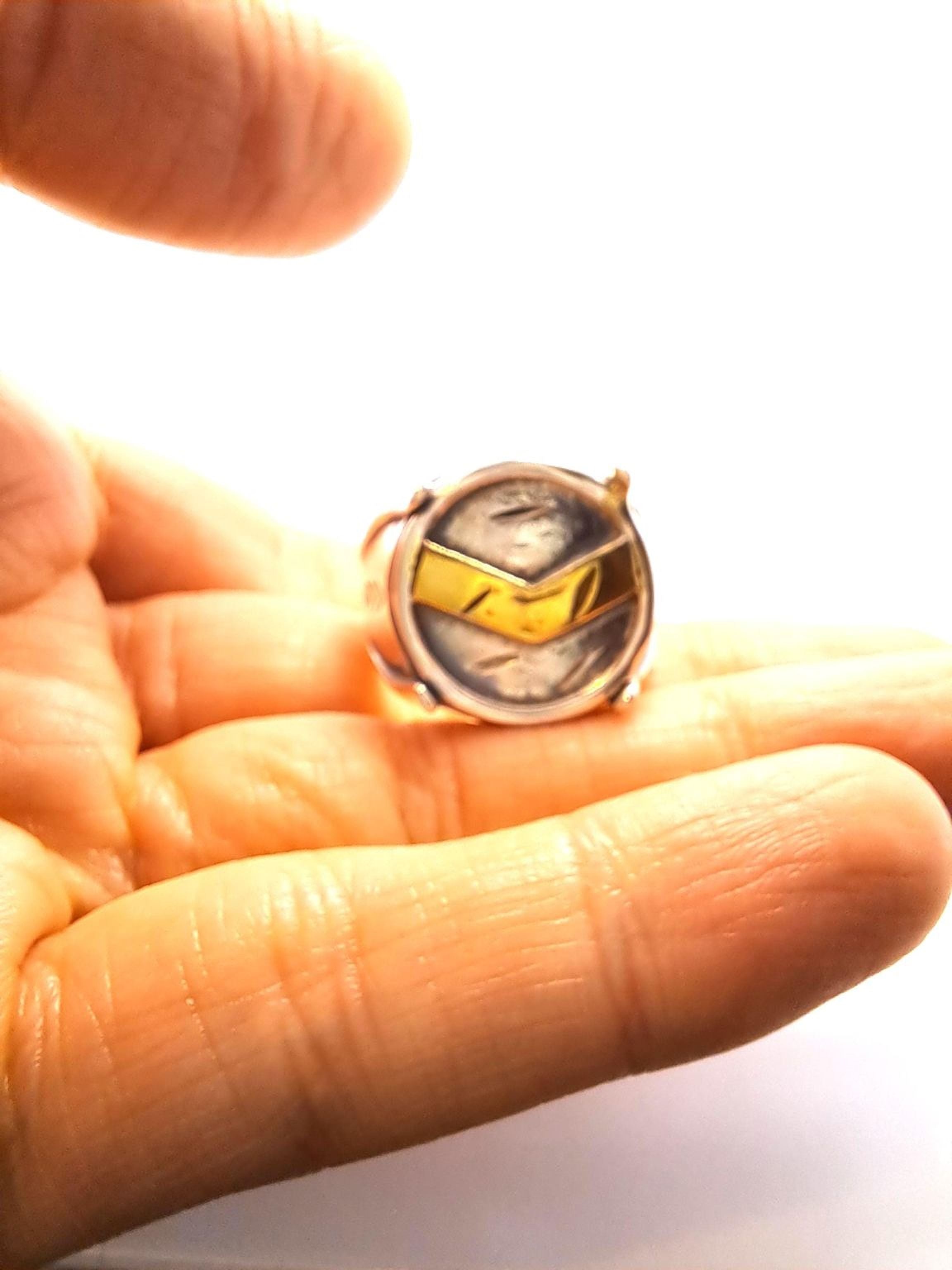 A hand holding a ring with a unique design, featuring a combination of gold and silver elements.
