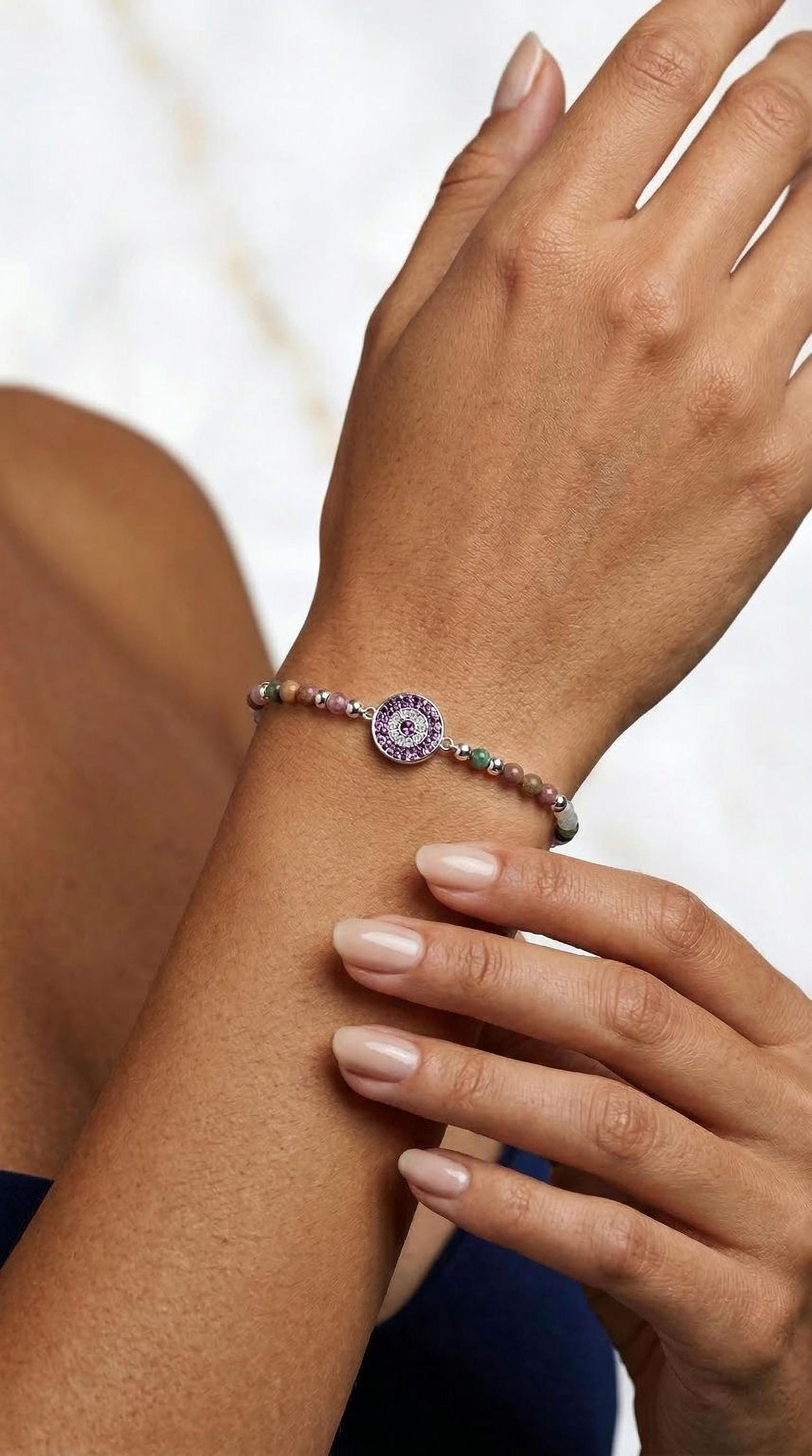 A close-up image of a person's hand wearing a bracelet with a charm on it.