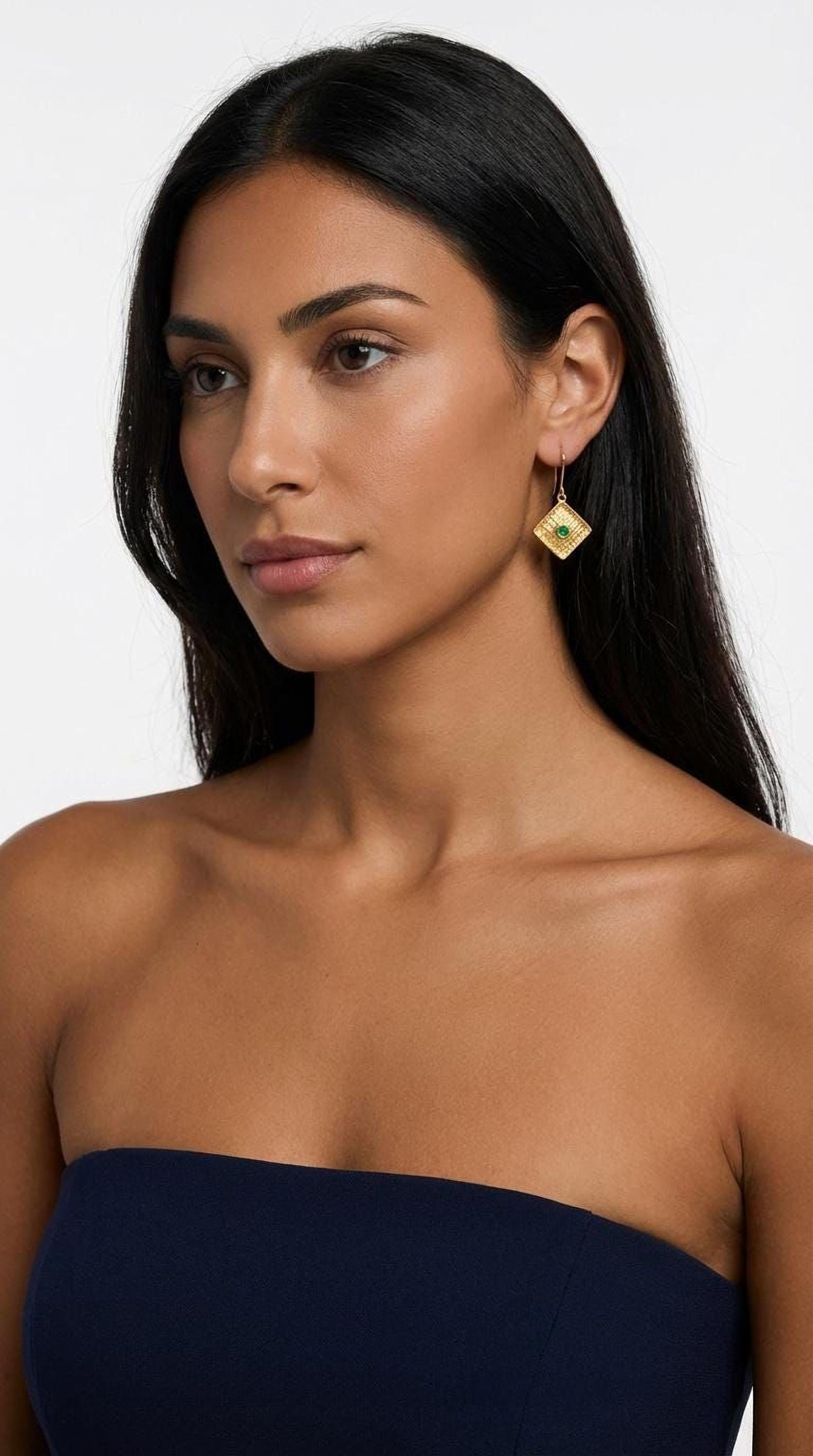 A woman with long dark hair wearing a navy blue strapless top and gold earrings with a diamond-shaped design.
