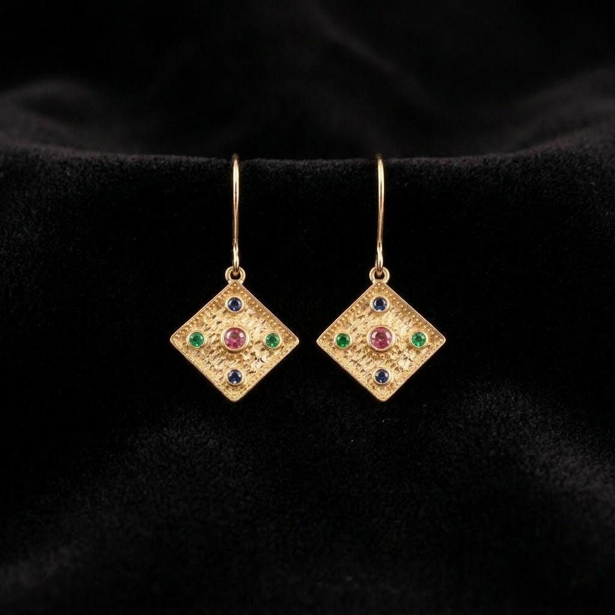 A pair of gold earrings with colorful gemstones, displayed against a black background.