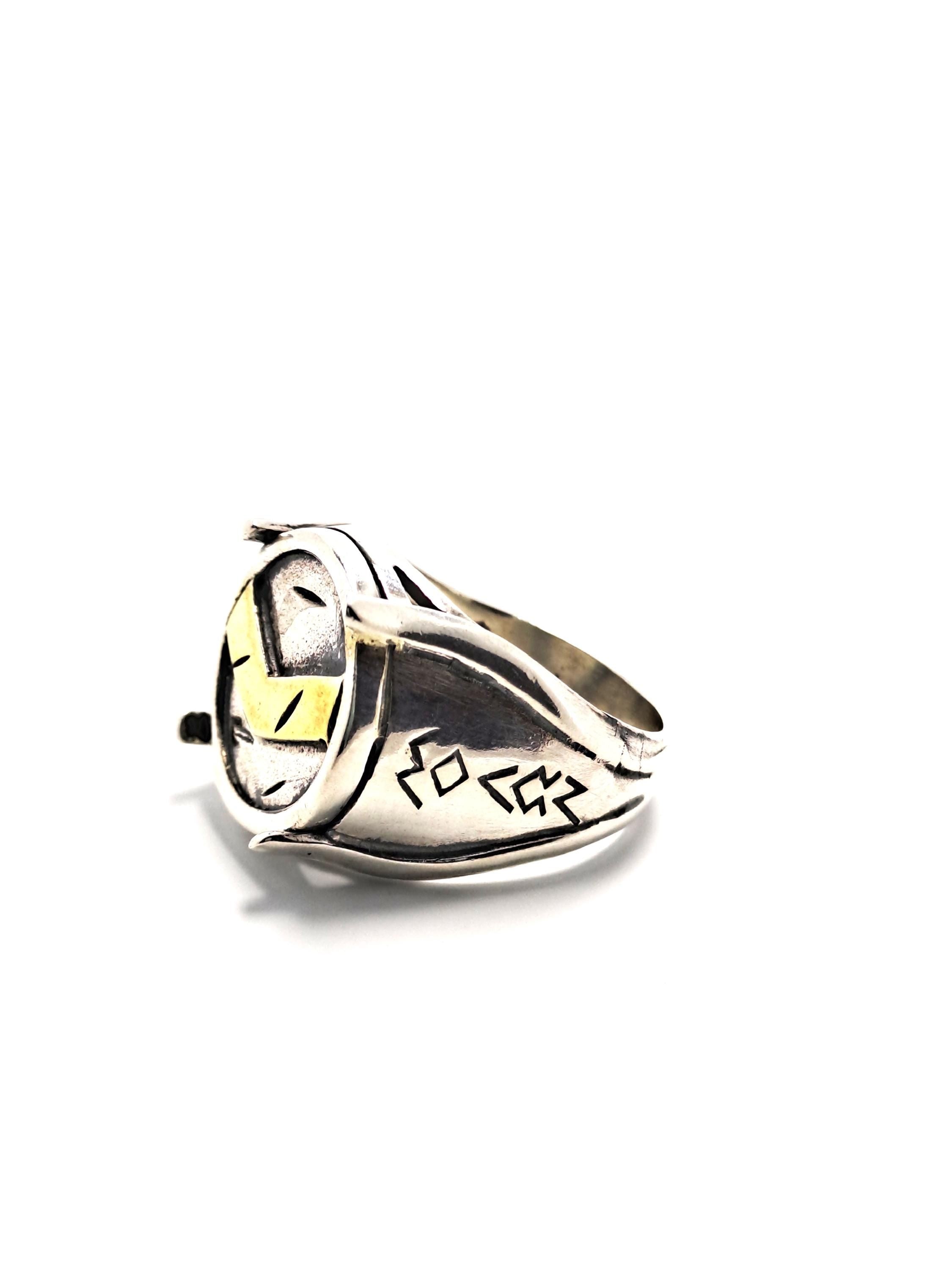 A silver ring with a yellow and black design on it, placed on a white background.