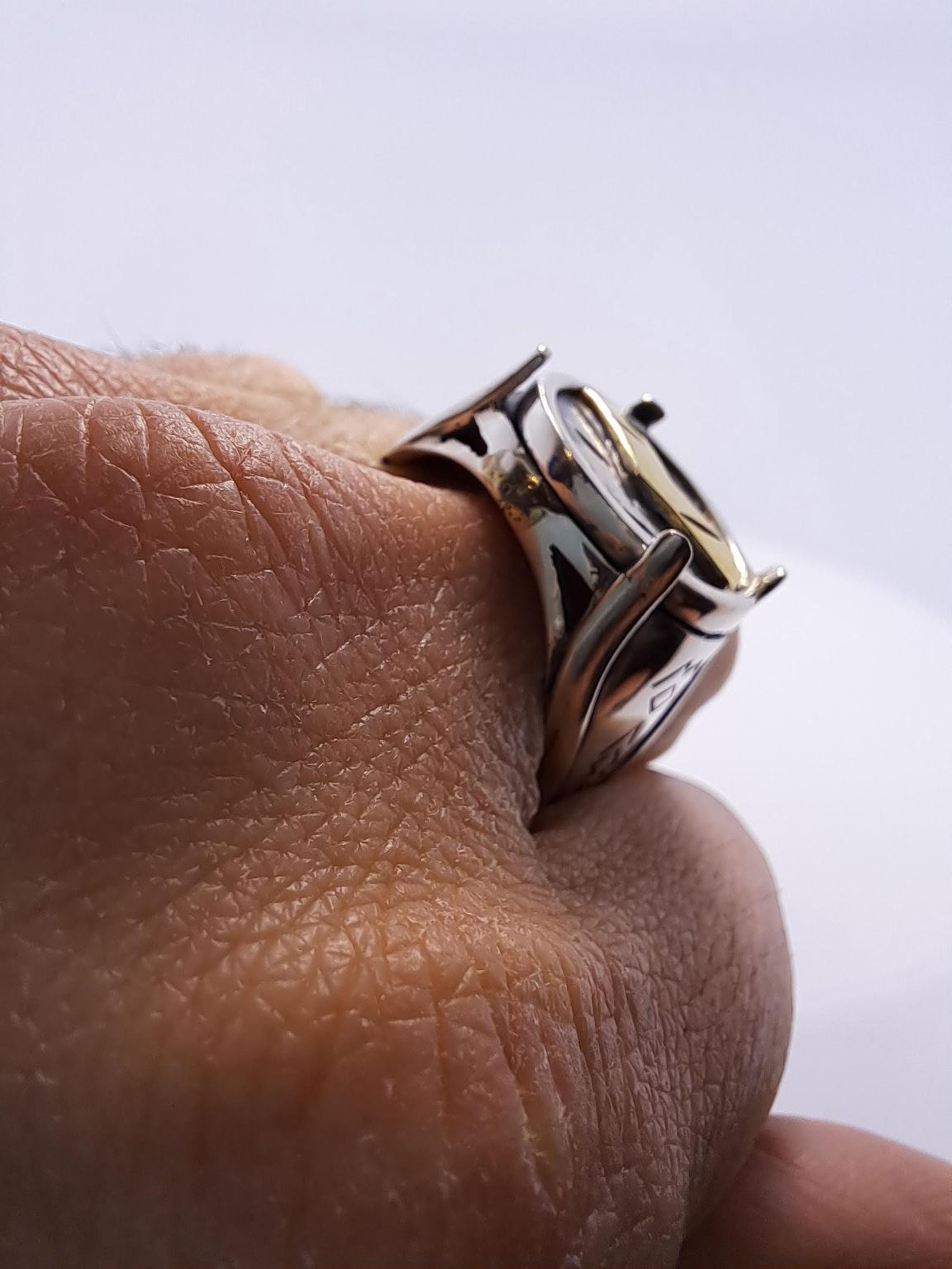 A close-up image of a person's hand wearing a silver ring with a unique design.