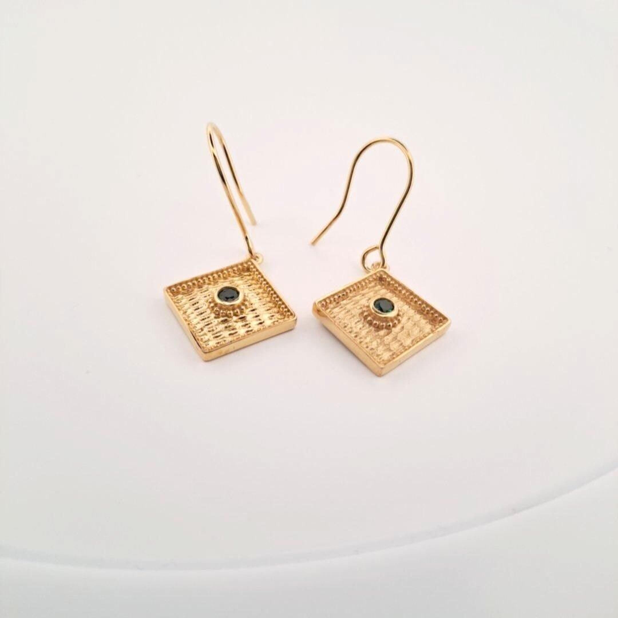 A pair of gold earrings with a diamond-shaped design and a small gemstone in the center.