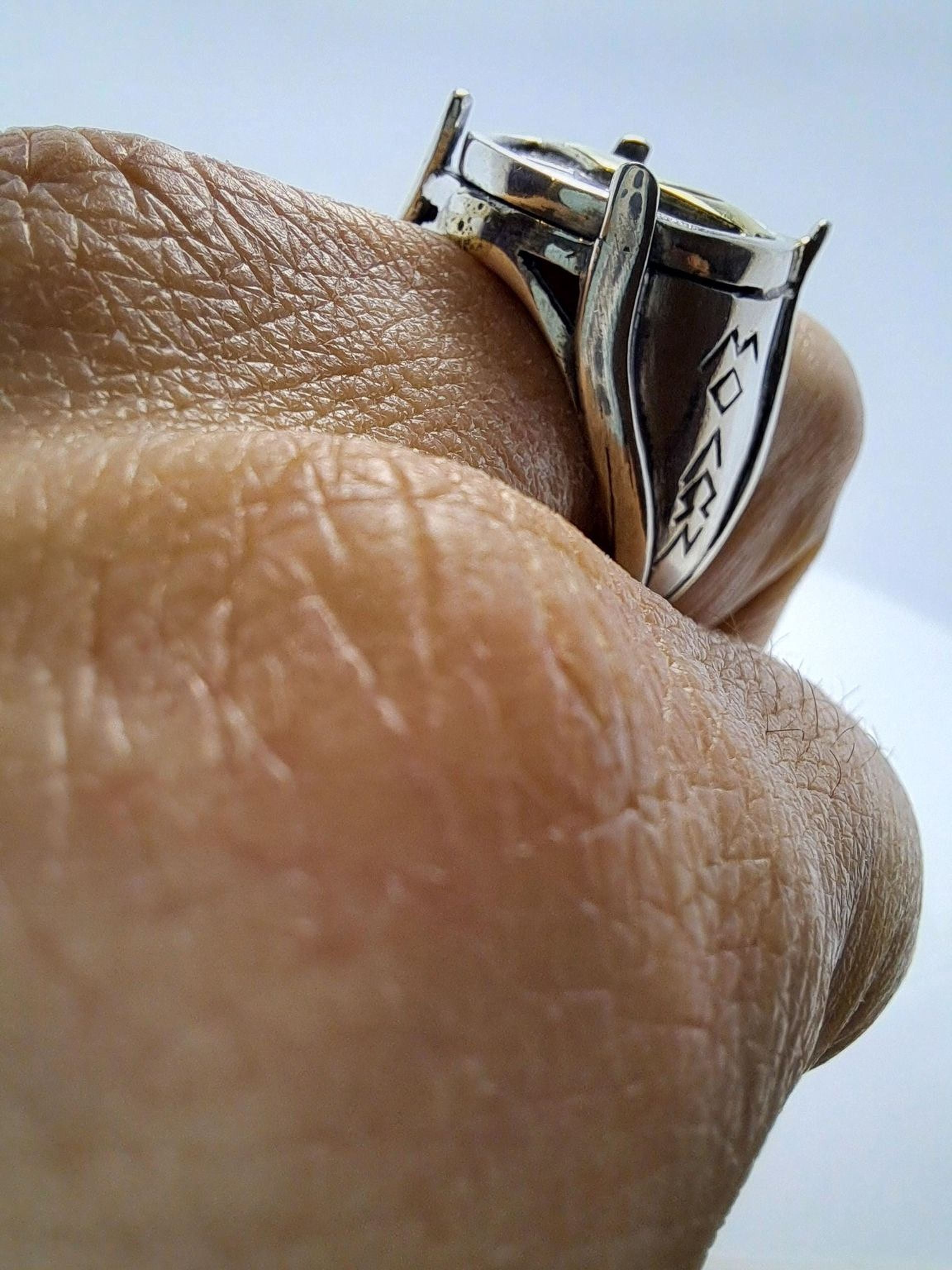 A close-up of a person's hand wearing a silver ring with a unique design.