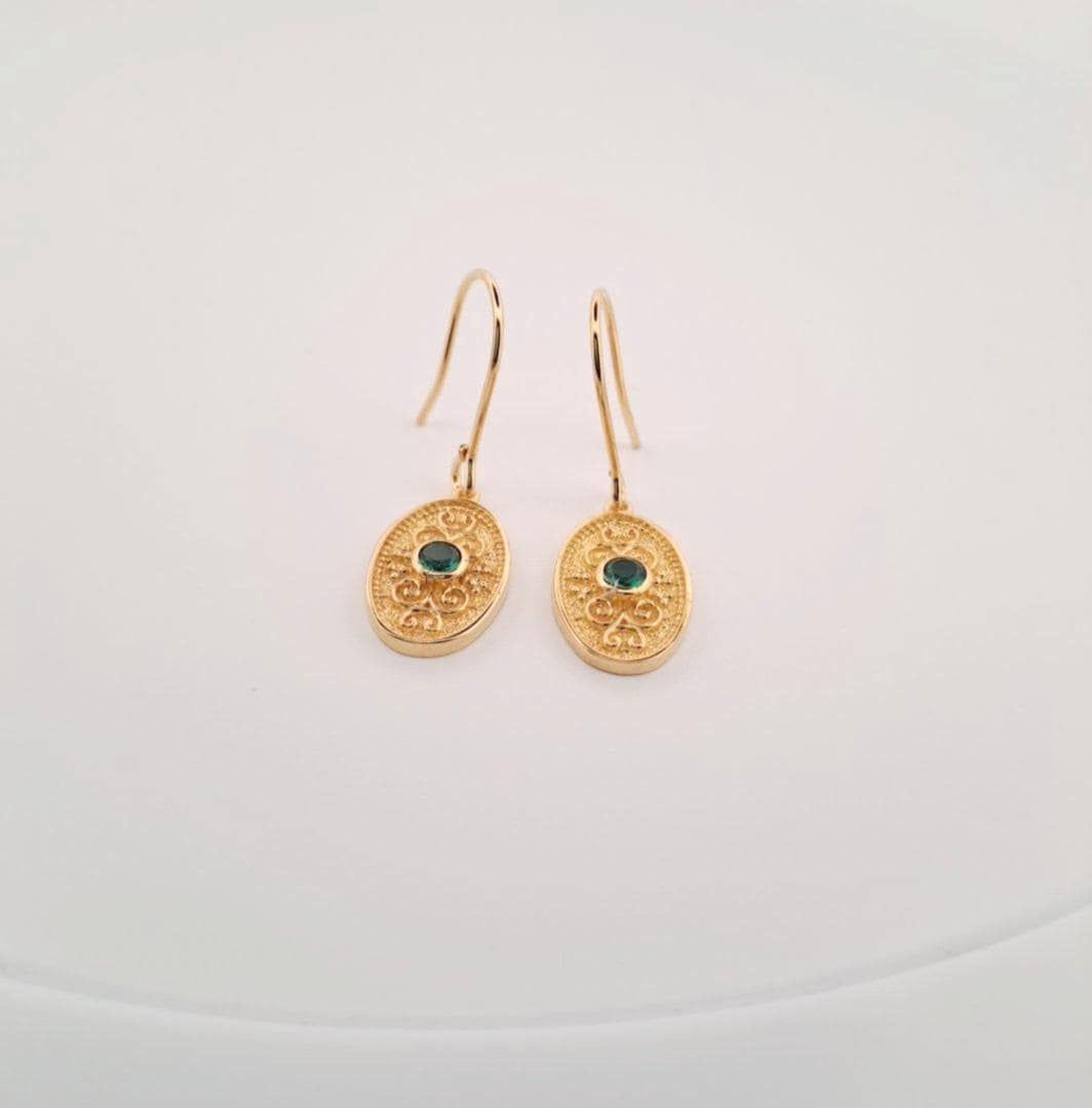 A pair of gold earrings with a green gemstone on a white background.