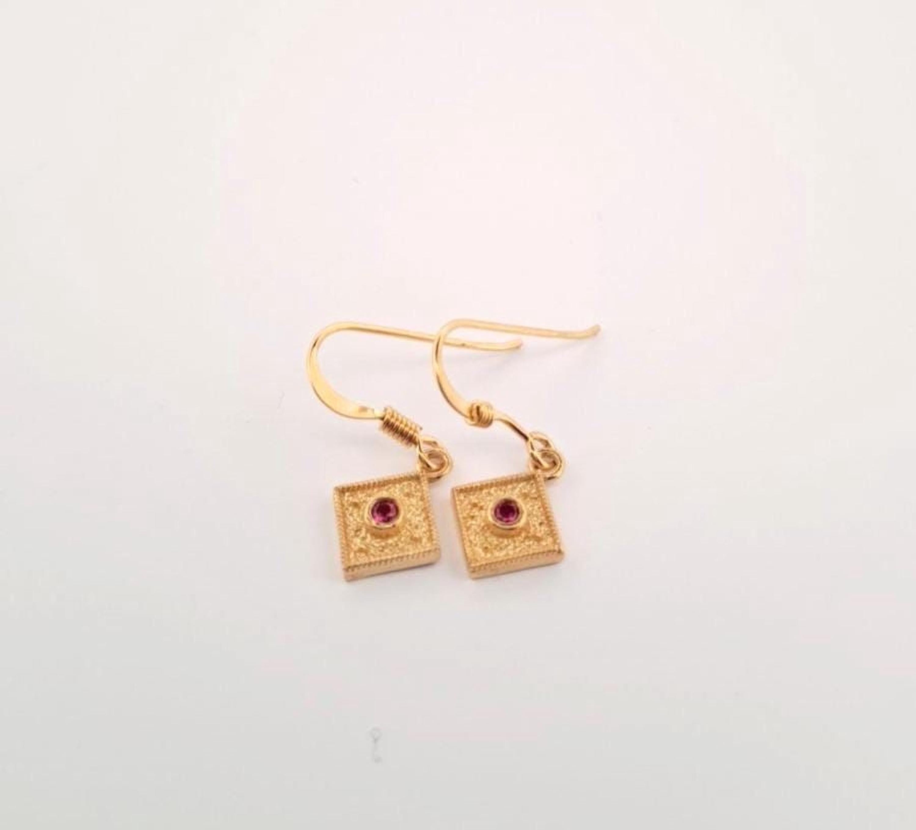 A pair of gold earrings with square pendants and a red gemstone.