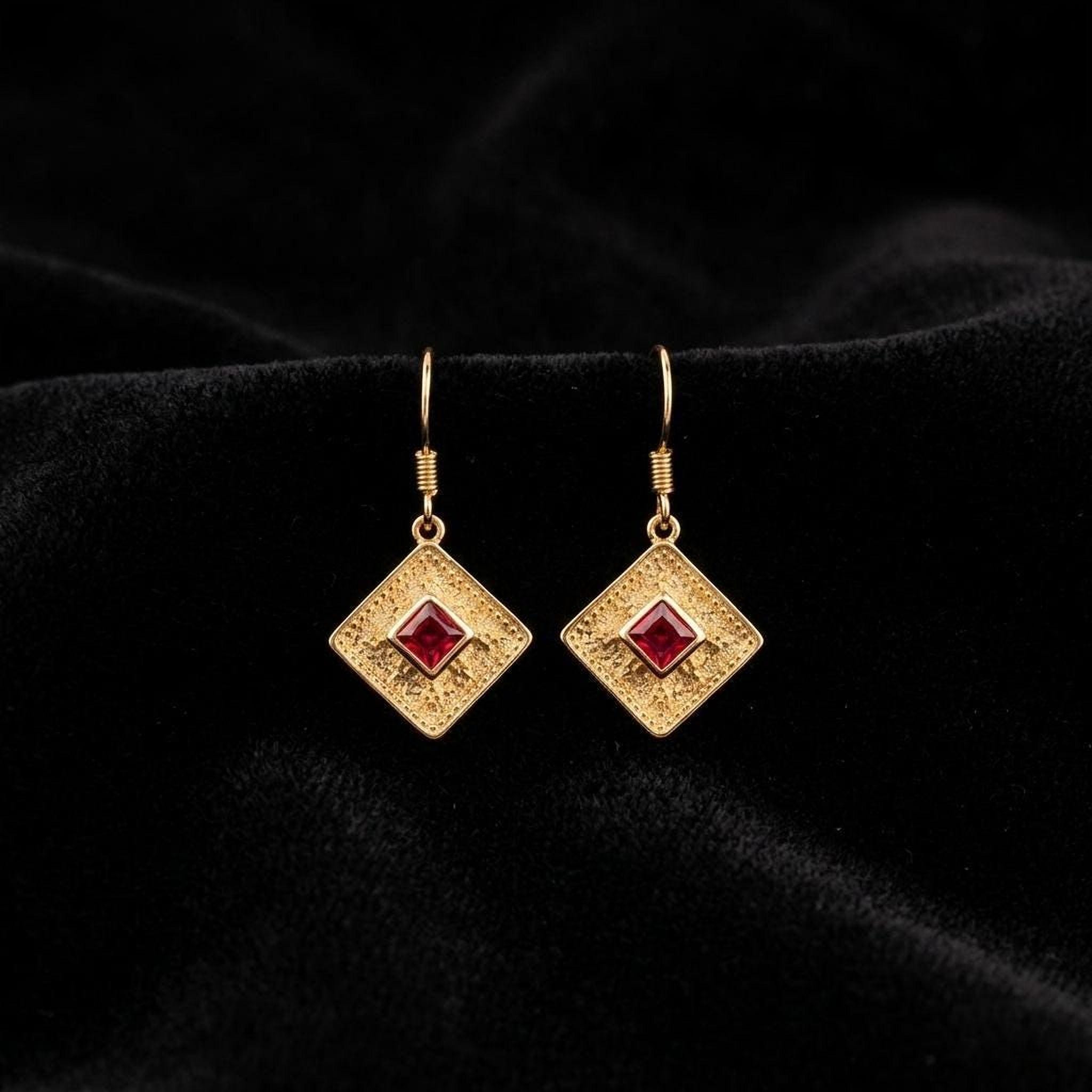 A pair of gold earrings with red gemstones, displayed on a black velvet background.