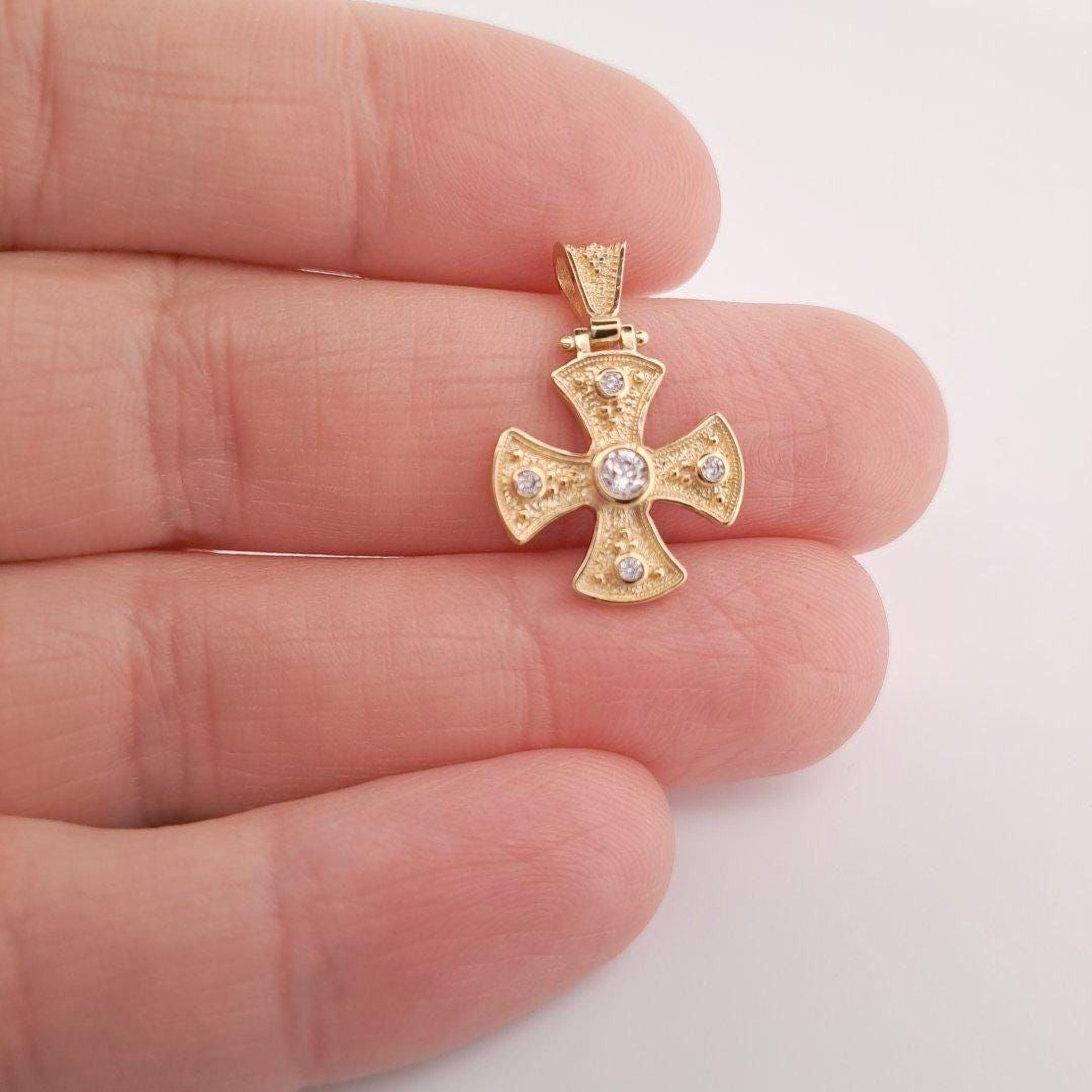 A hand holding a small gold cross pendant with a diamond in the center.