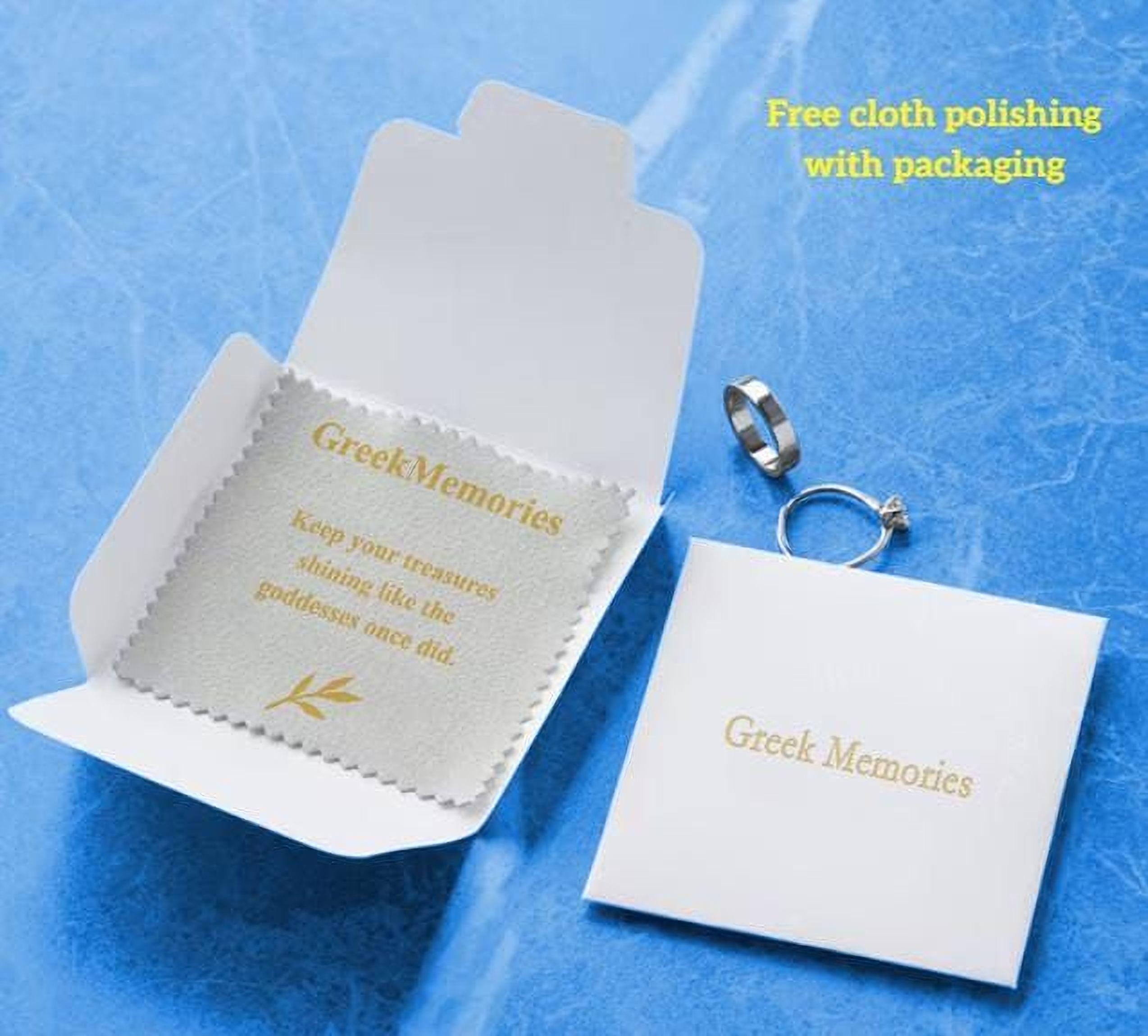 a white box with a label, a silver ring, and a white cloth with a message about Greek Memories.