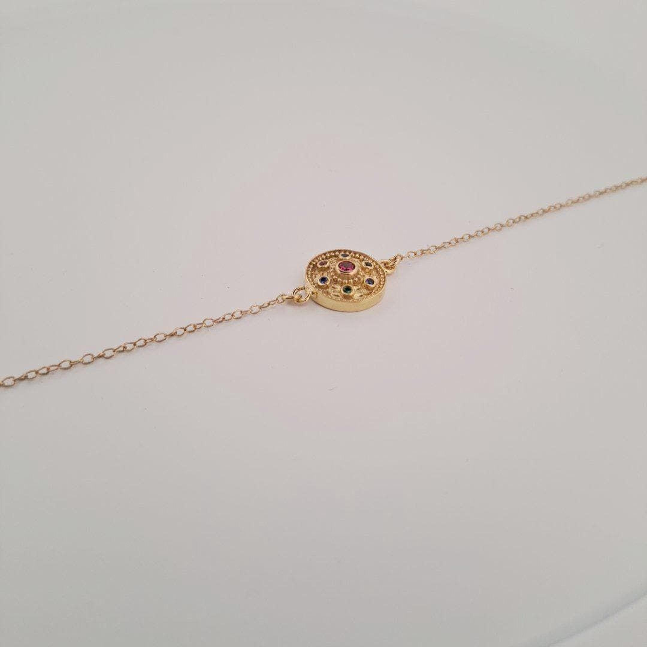 A gold-colored necklace with a circular pendant featuring a gemstone in the center.