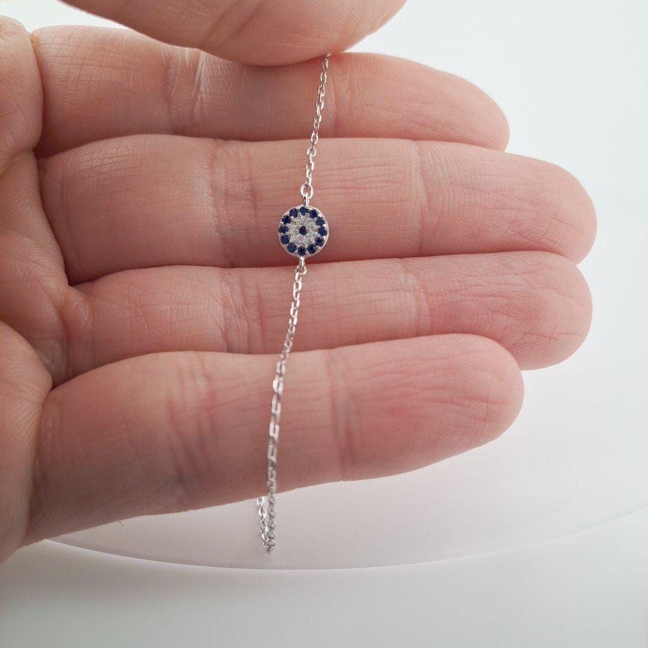 A hand holding a delicate silver necklace with a small blue and white charm.