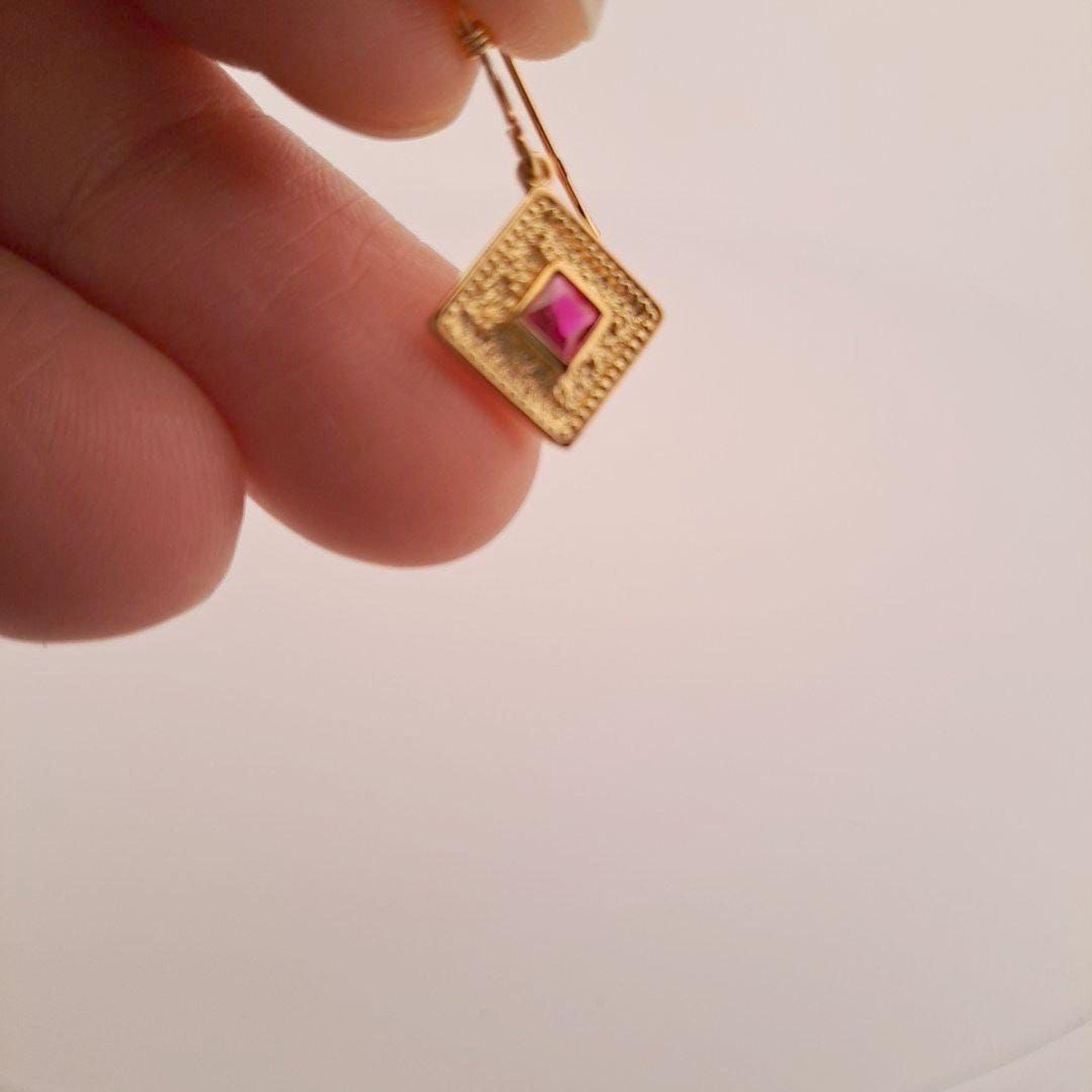A hand holding a small gold earring with a pink gemstone.