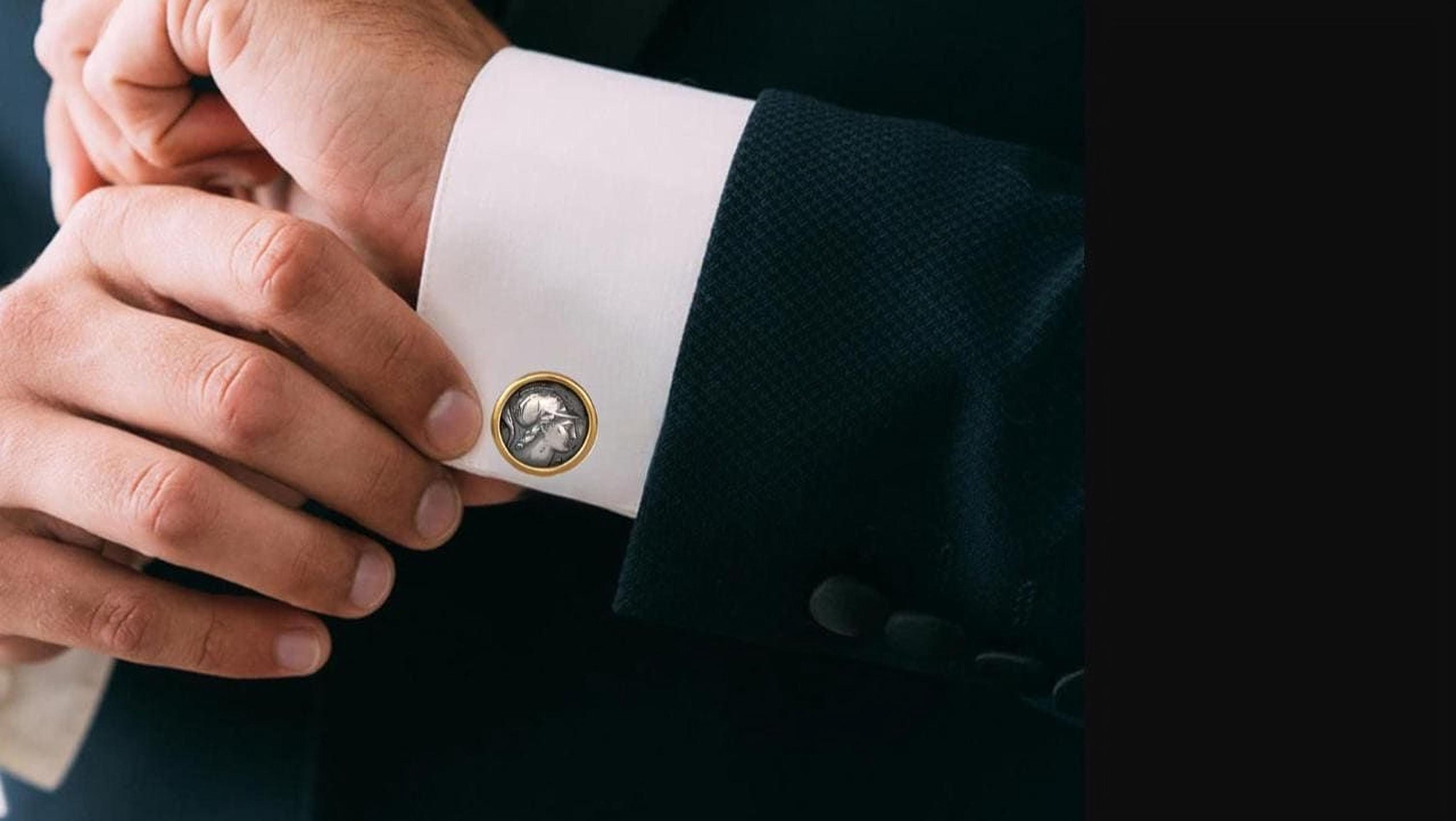A close-up of a person's hand adjusting a cufflink with a small, ornate design on it.
