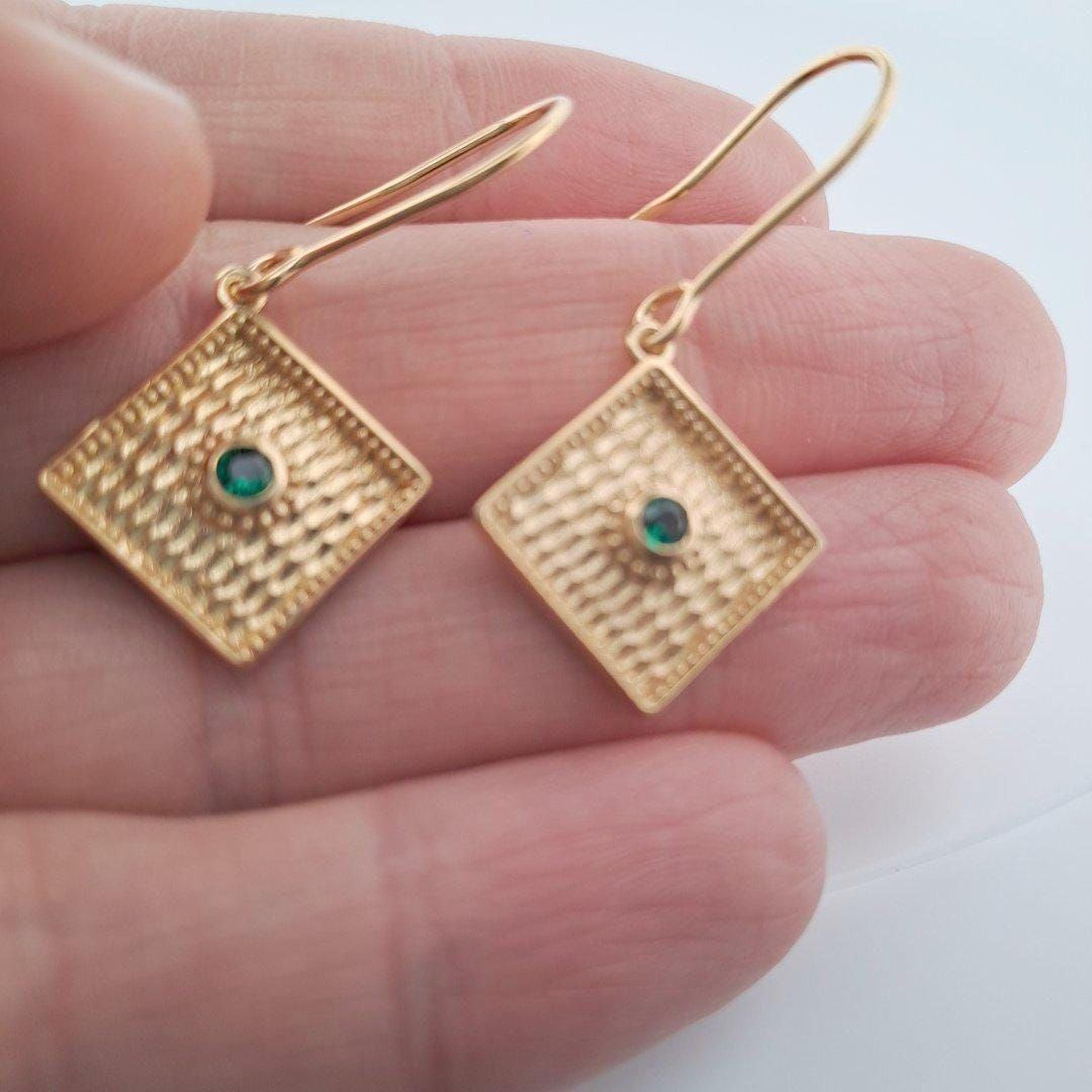 A hand holding a pair of gold earrings with a green gemstone.
