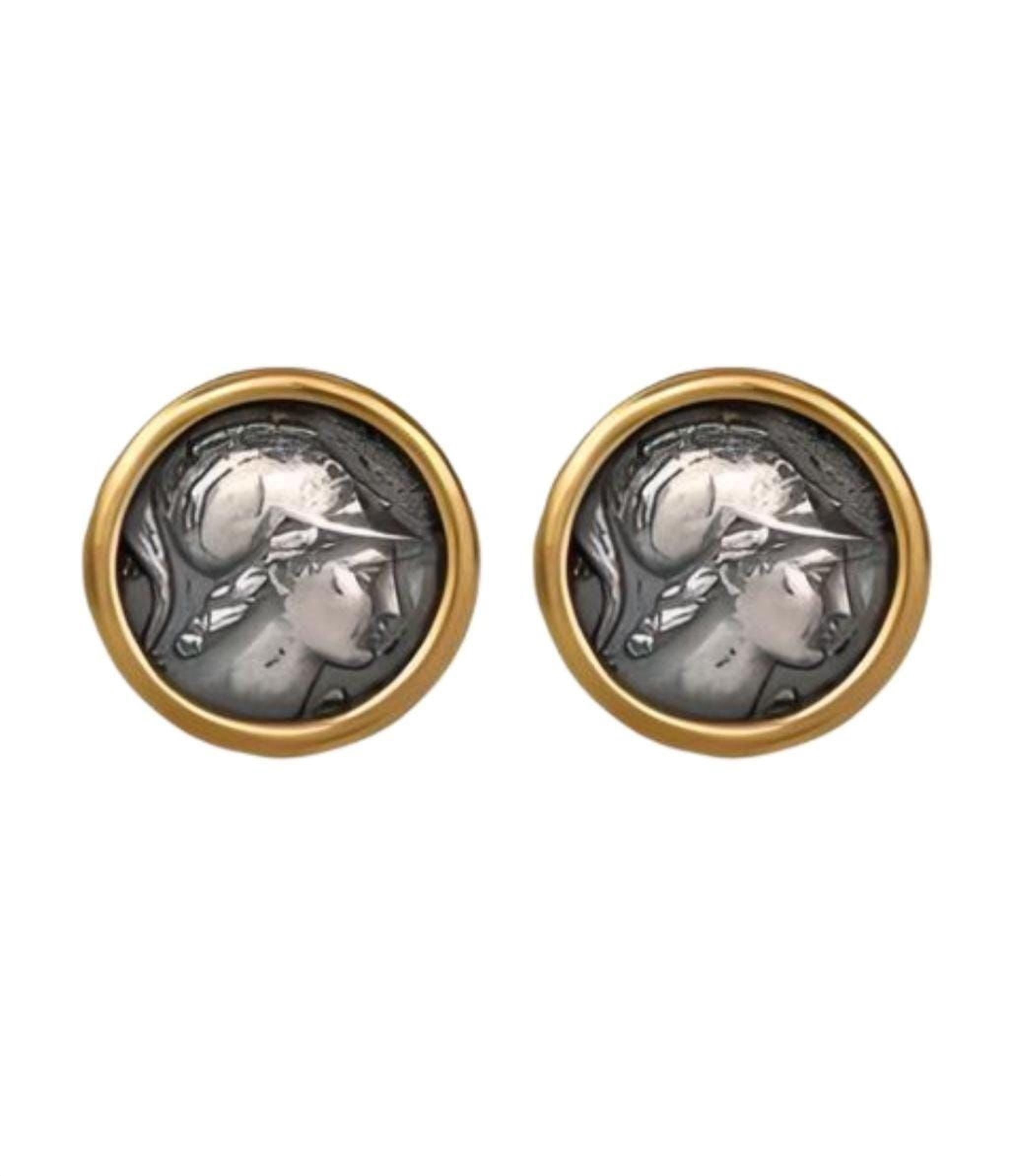 two round earrings with a silver-colored design, possibly depicting a woman's face, encased in a gold-colored frame.